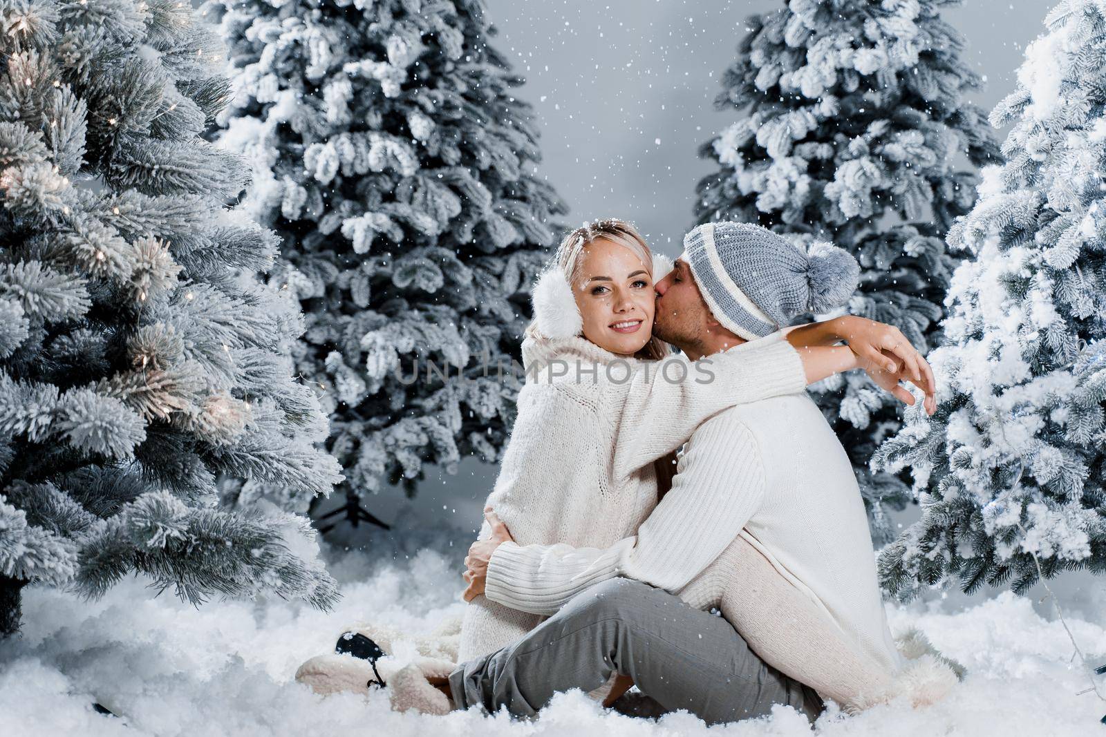 Winter love story at the eve of new year celebration. Couple hugging near christmass trees. Winter holidays. Love story of young couple weared white pullovers. Happy man and woman love each other by Rabizo