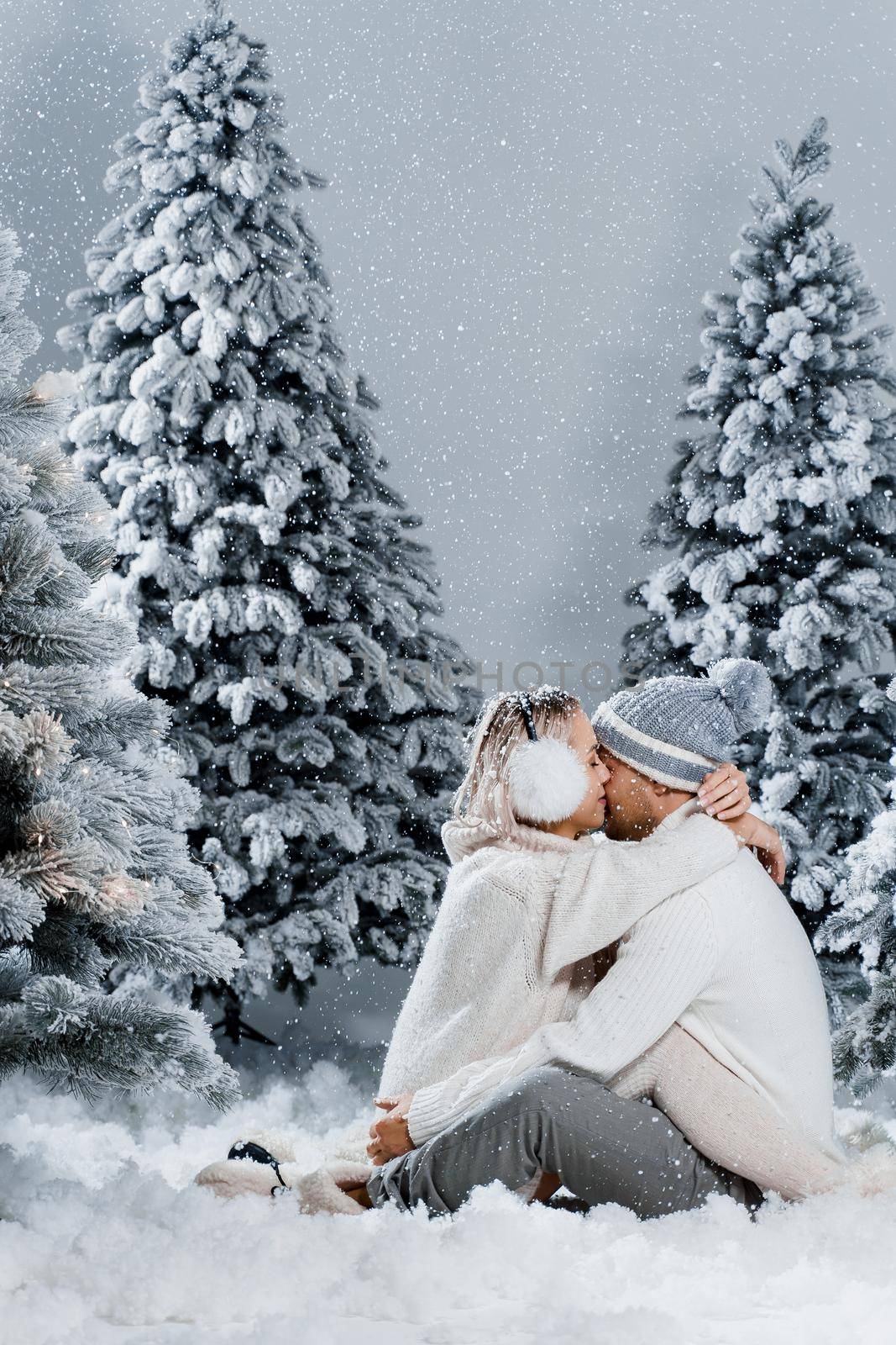 Couple hugging near christmass trees. Winter holidays. Love story of young couple weared white pullovers. Happy man and young woman love each other by Rabizo