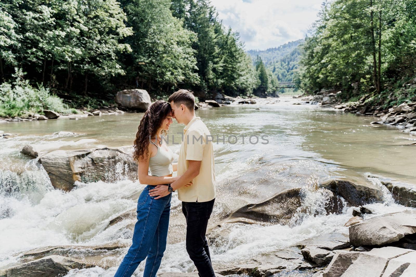 Love story of couple. Travelling in Karpathian mountains. Waterfall in mountain river. Cascade waterfall and happy couple hugging each other
