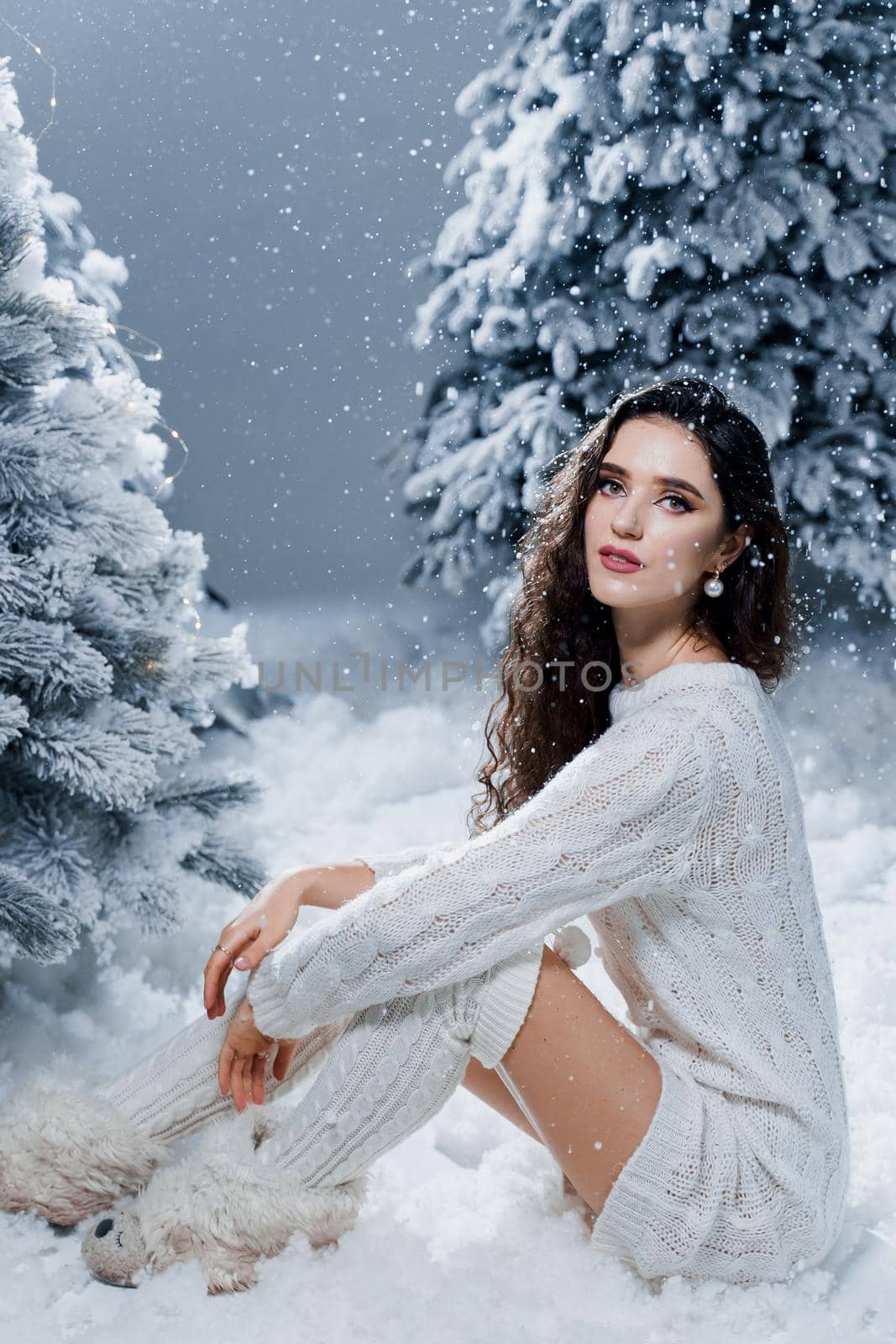 Attractive girl in a warm white sweater and white socks near snowy trees before the new year. Christmas holiday.