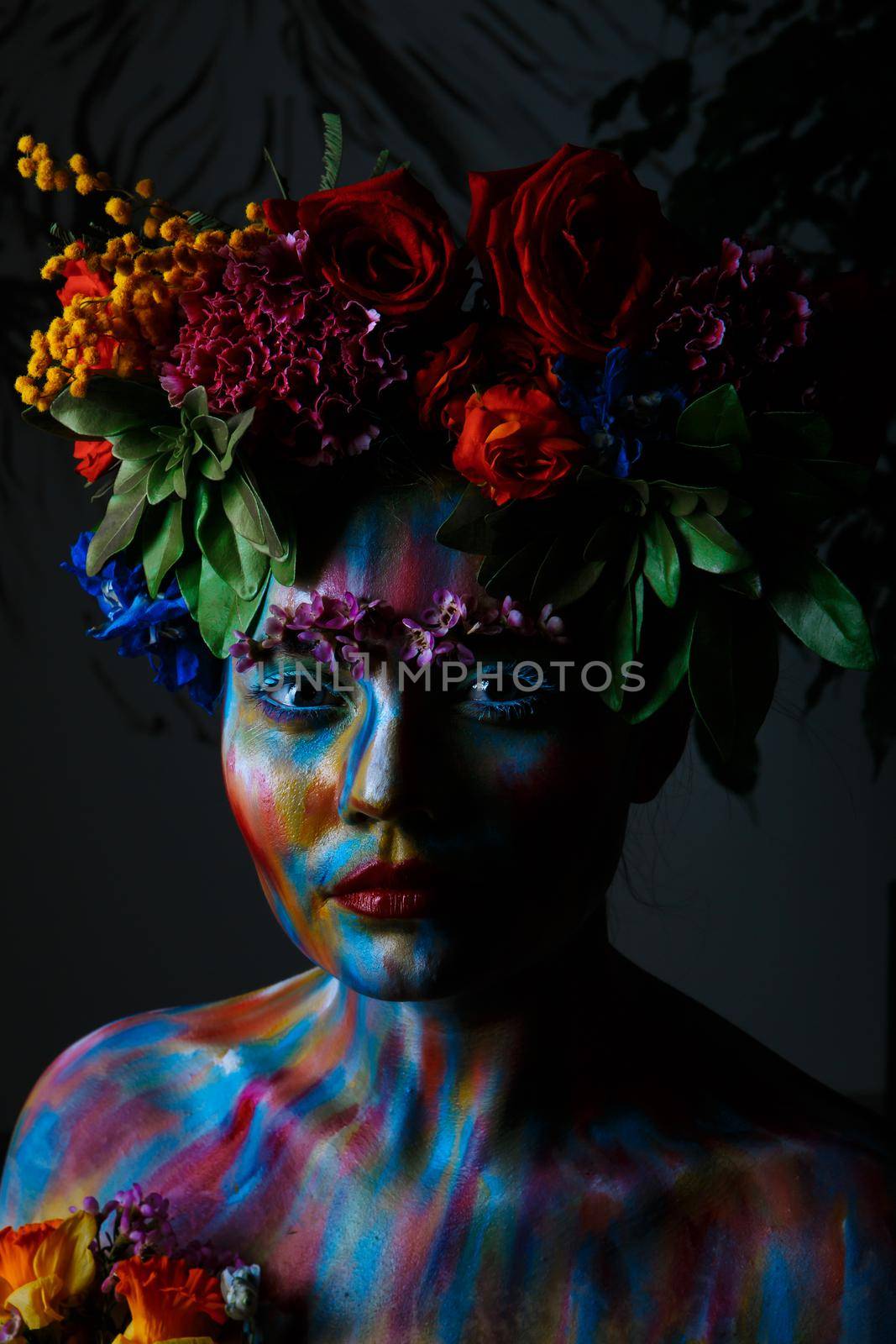 Portrait of a girl whose face is painted with colored paints in a wreath of flowers.
