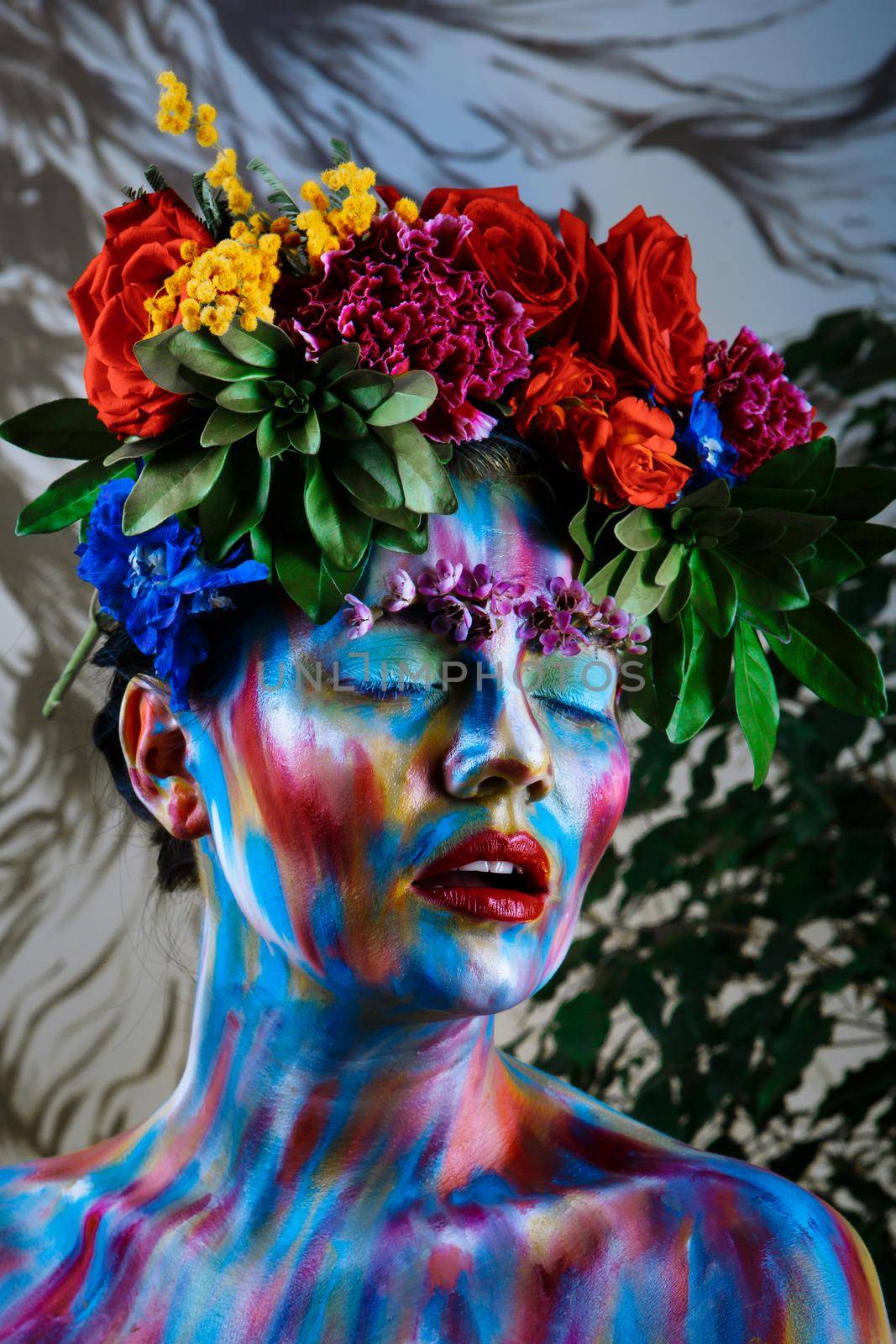 Portrait of a girl whose face is painted with colored paints in a wreath of flowers.