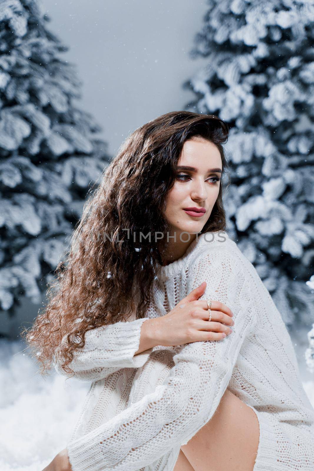 Attractive girl in a warm white sweater and white socks near snowy trees before the new year. Christmas holiday by Rabizo