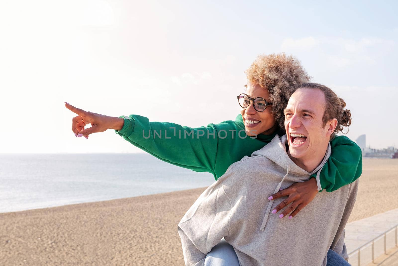 smiling young latin woman piggyback with her boyfriend having fun, concept of friendship and couple relationship, copy space for text