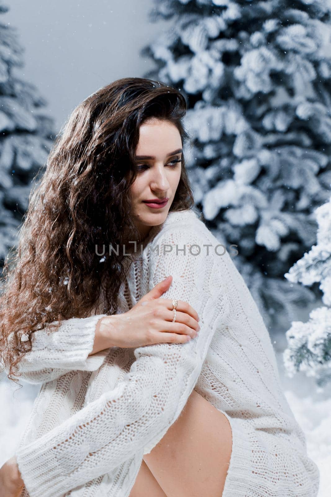 Attractive girl in a warm white sweater and white socks near snowy trees before the new year. Christmas holiday by Rabizo