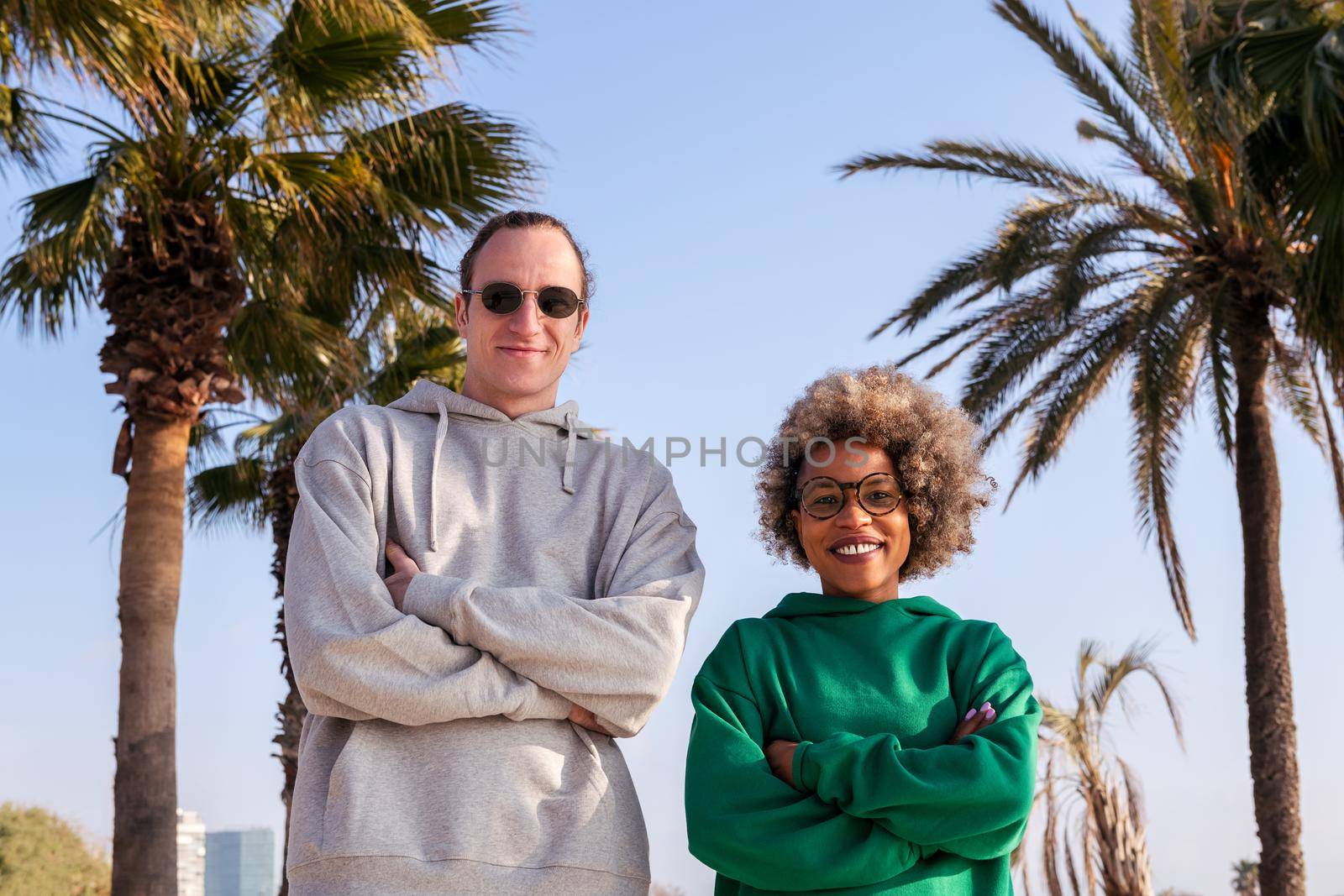 couple of friends with arms crossed smiling happy looking at camera next to palm trees, concept of friendship and couple relationship