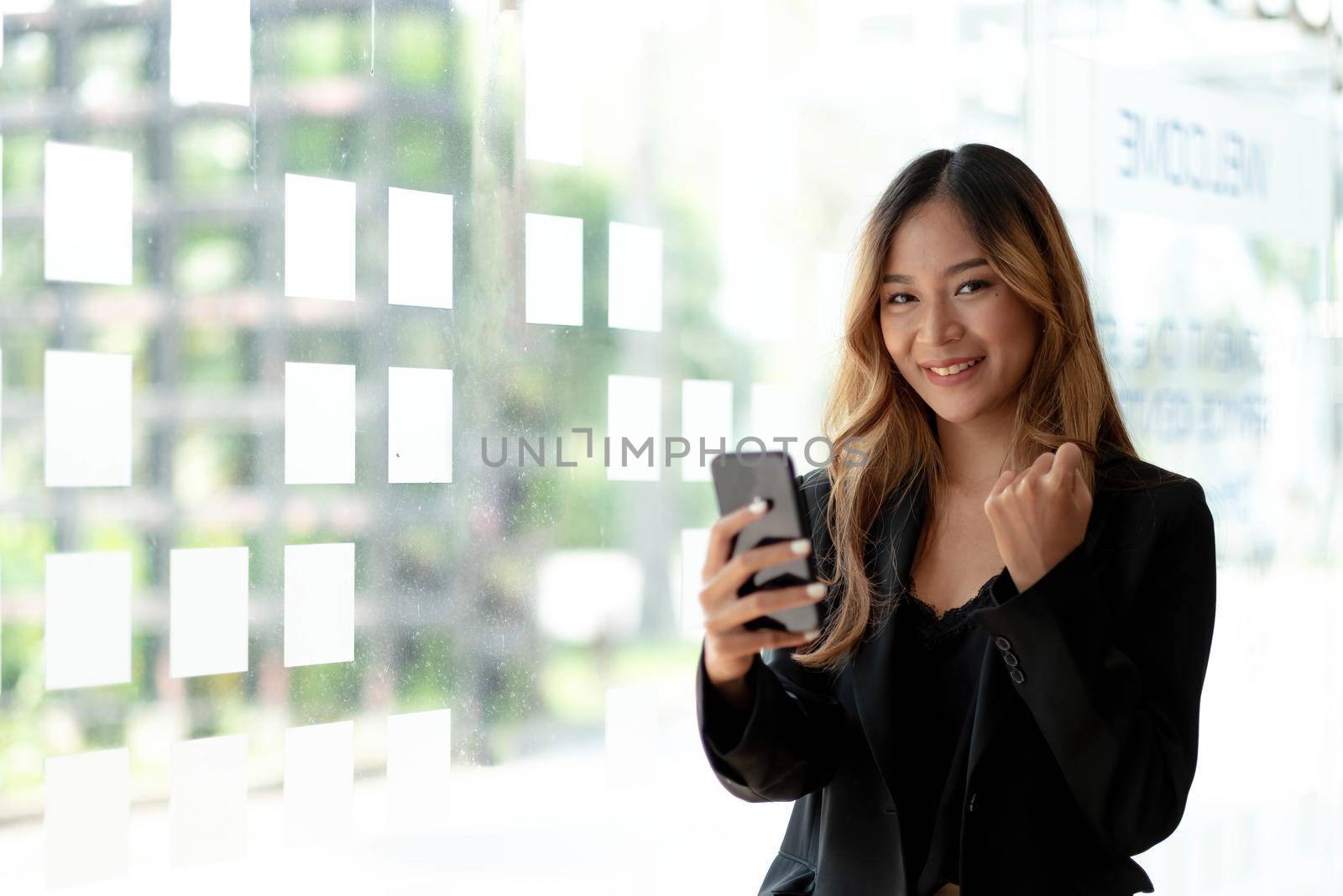 Beautiful asian woman using smartphone, exciting and celebrating with good news of business successful. Small business startup concept. by wichayada