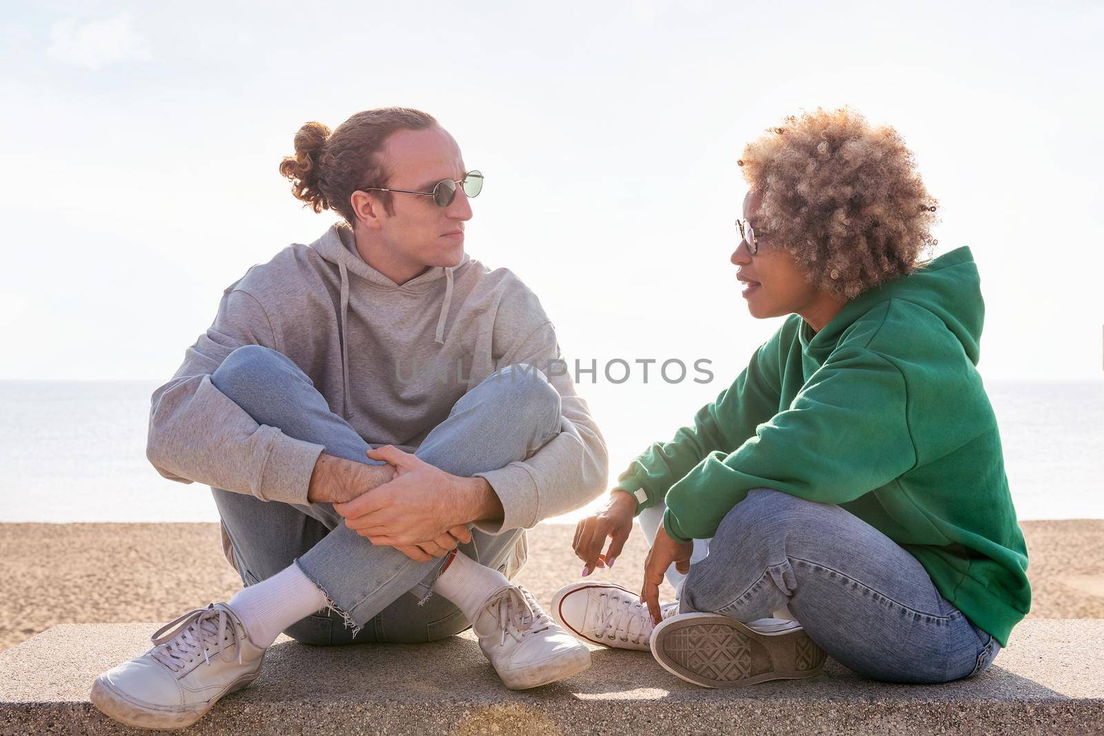 young couple chatting at sunset seated on a bench by the beach, concept of friendship and communication in a relationship