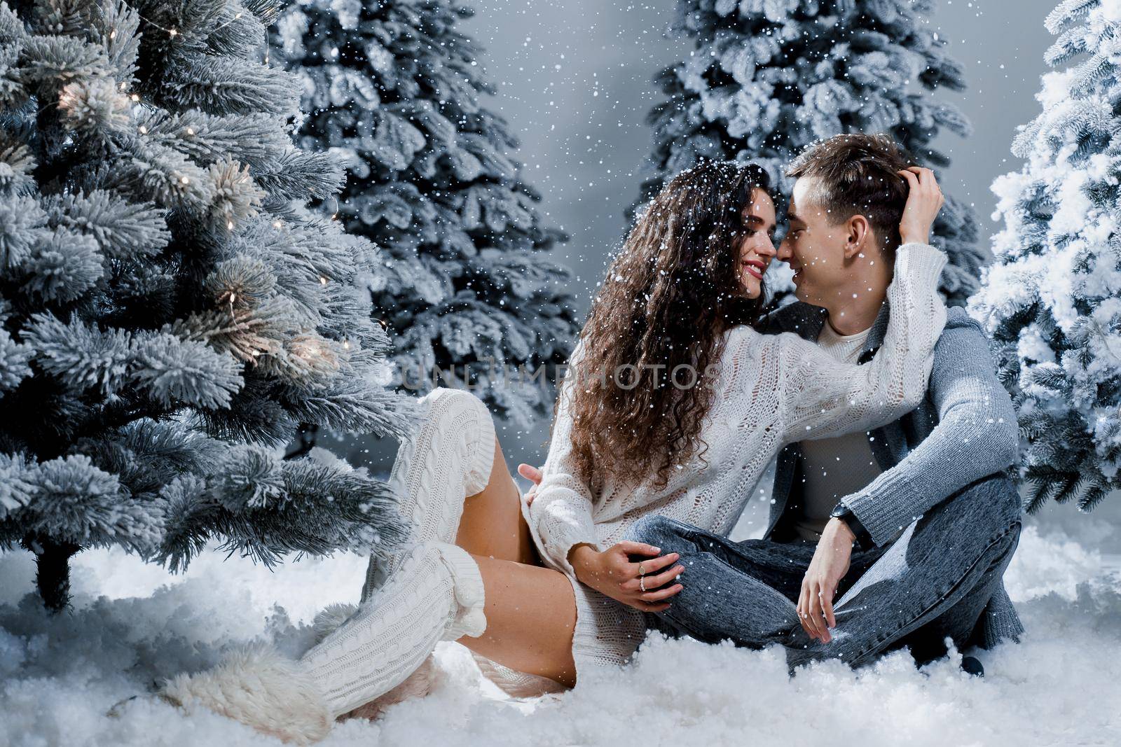New year love story. Couple kiss and hug, snow is falling. Happy young couple near christmas trees in winter day.