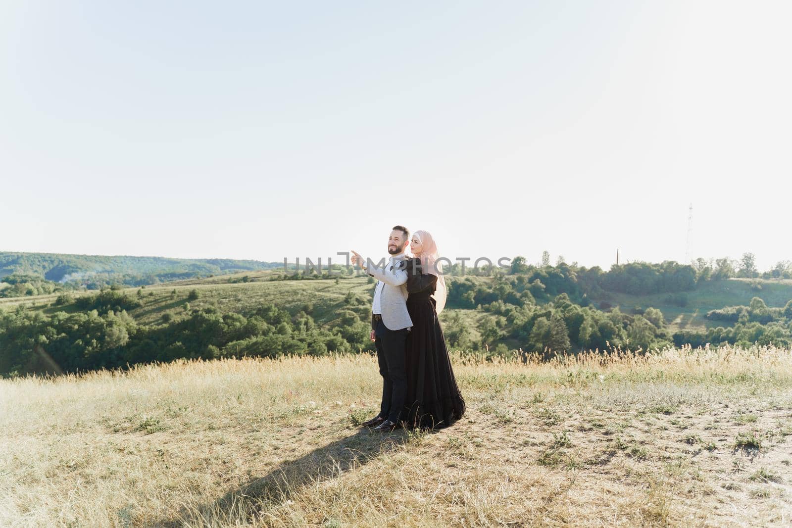 Muslim love story of mixed couple. Man and woman smiles and walks on the green hills . Woman weared in hijab looks to her man. Advert for on-line dating agency