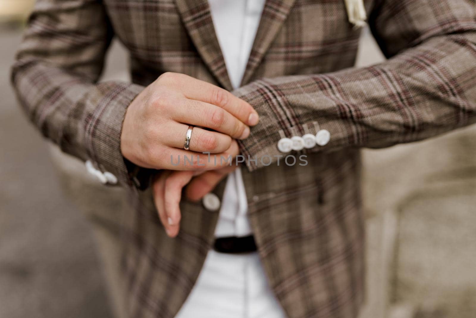 Groom in brown plaid jacket looks at his ring on the finger. Advert for wedding agency