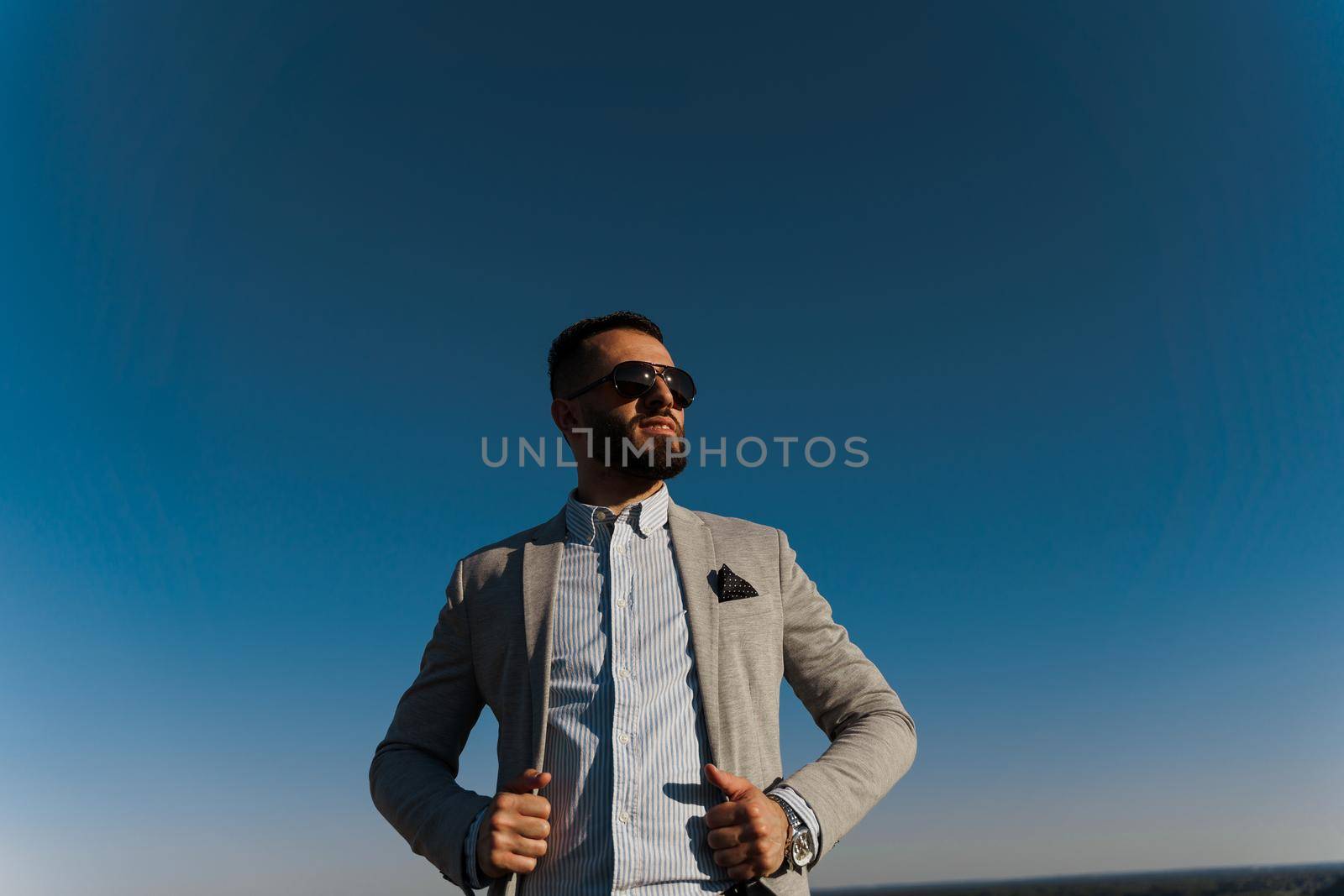 Handsome bearded arabian man in sunglasses on the blue sky background. Confident muslim business man. Arab man weared in grey coat