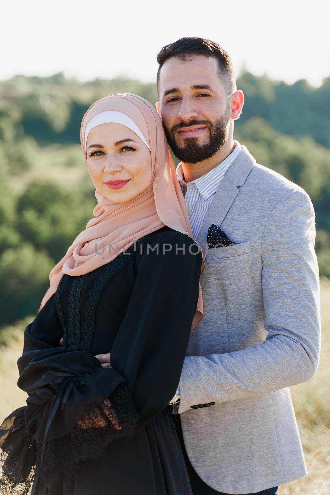 Muslim love story close-up. Mixed couple smiles and hugs on the green hills . Woman weared in hijab looks to her man. Advert for on-line dating agency. by Rabizo