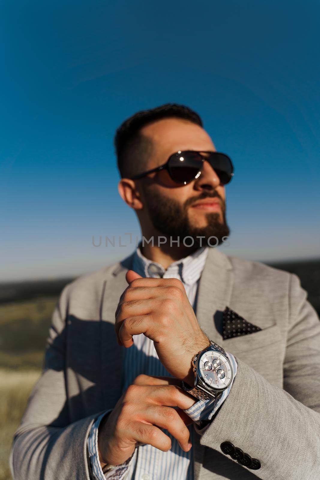 Handsome bearded arabian man in sunglasses on the blue sky background. Confident muslim business man. Arab man weared in grey coat