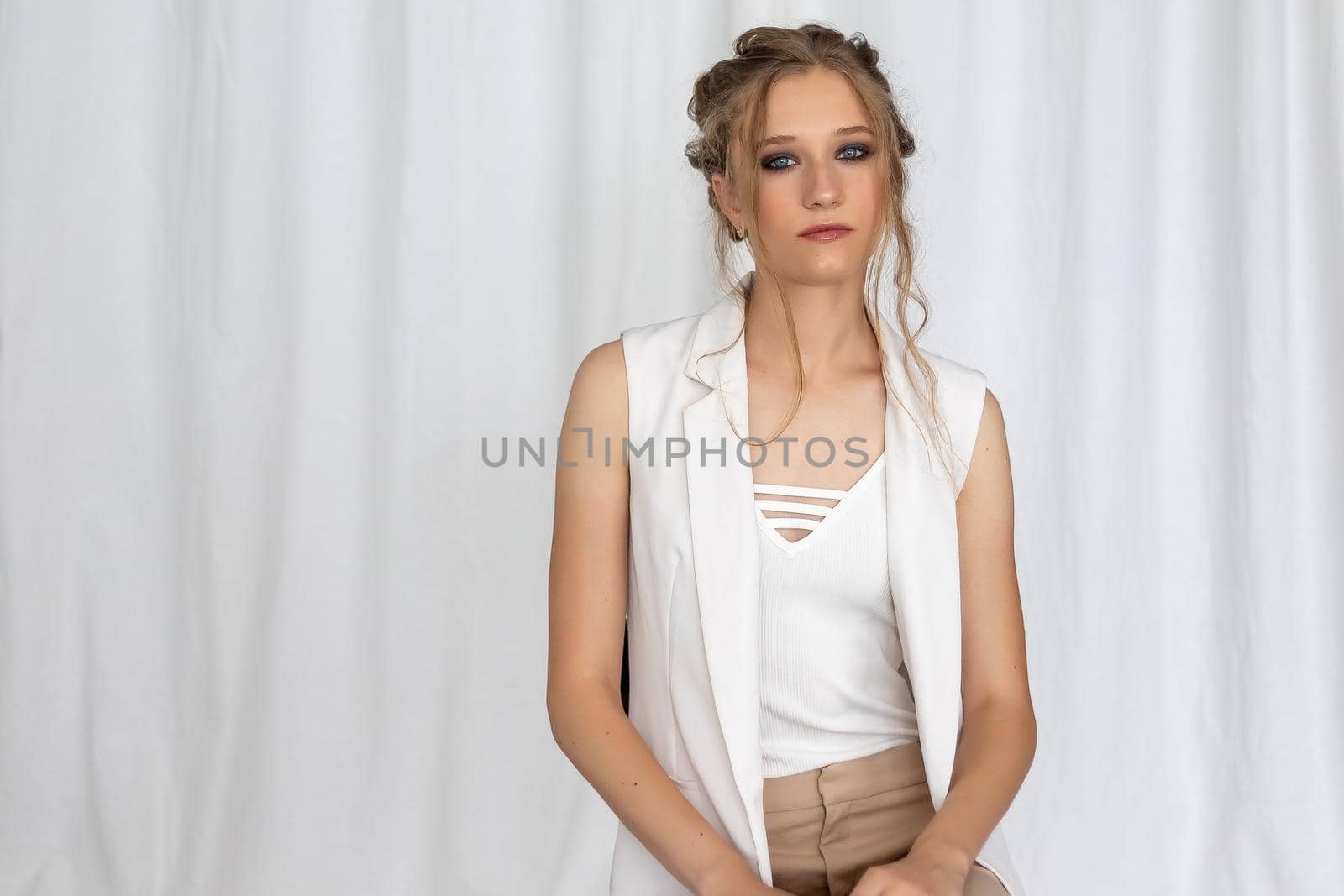 Young attractive woman in white clothes posing on abstract pale background looking at camera confident. Soft sunny colors. Beauty concept by Anyatachka