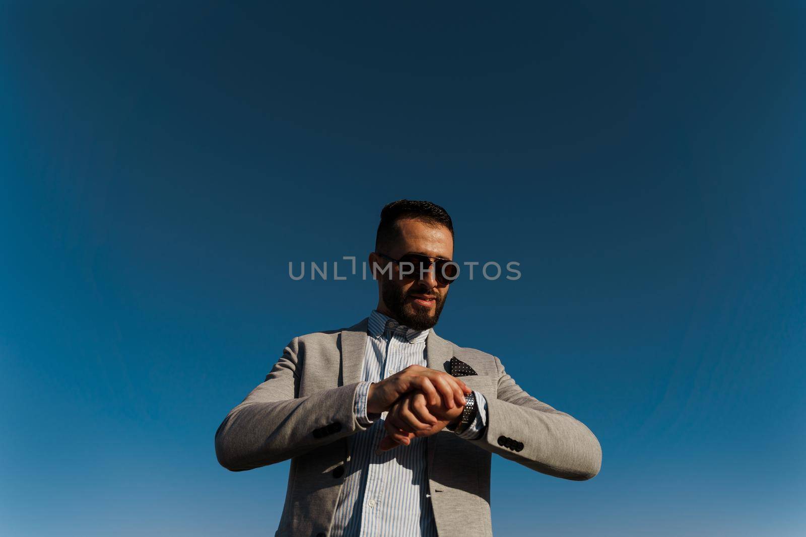 Handsome bearded arabian man in sunglasses on the blue sky background. Confident muslim business man. Arab man weared in grey coat. by Rabizo