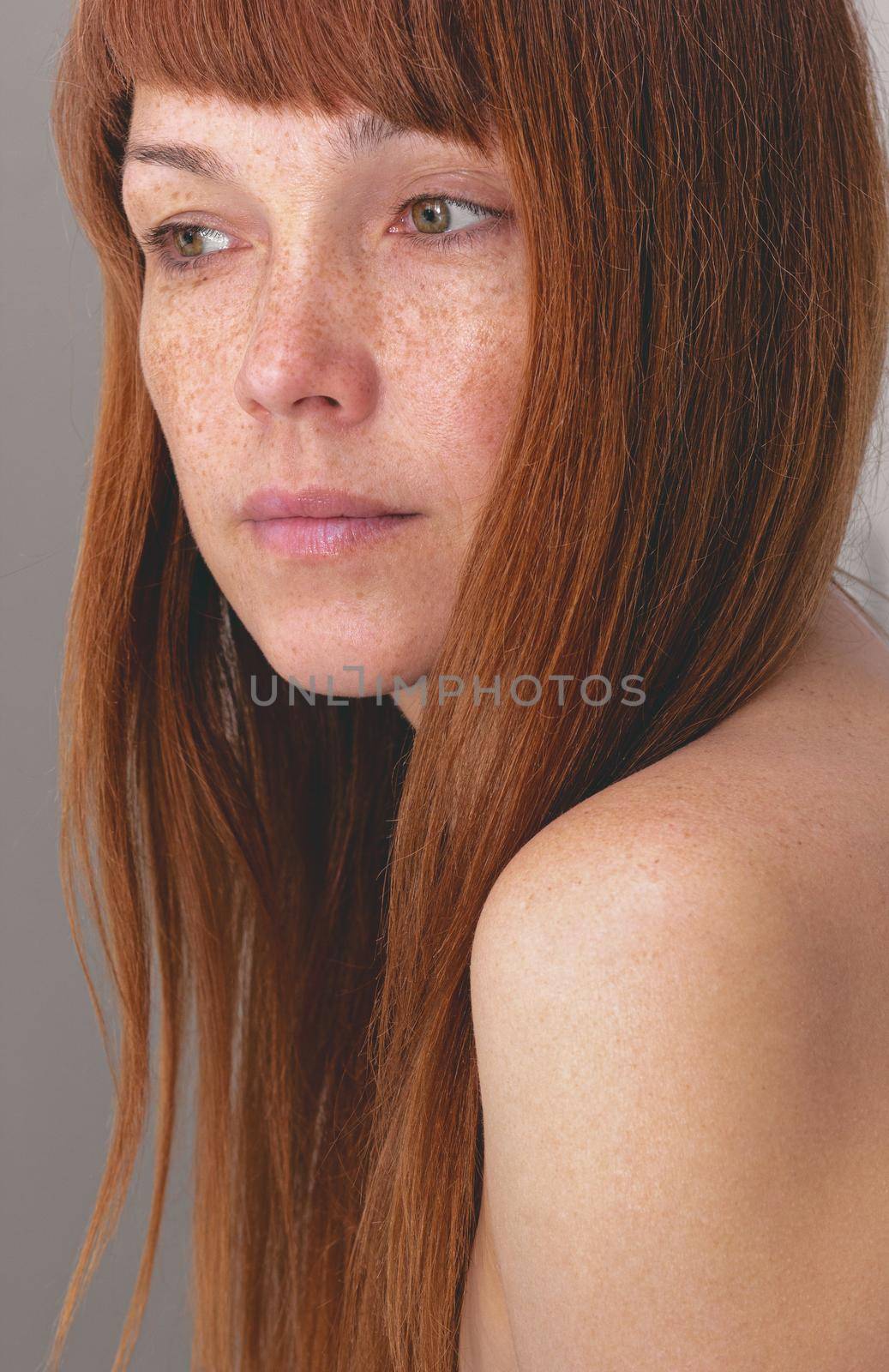 Portrait of caucasian middle-aged woman with reddish hair and freckles looking aside over gray background