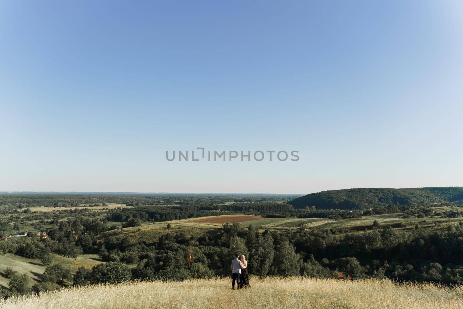 Muslim love story. Mixed couple smiles and hugs on the green hills . Woman weared in hijab looks to her man. Advert for on-line dating agency. by Rabizo