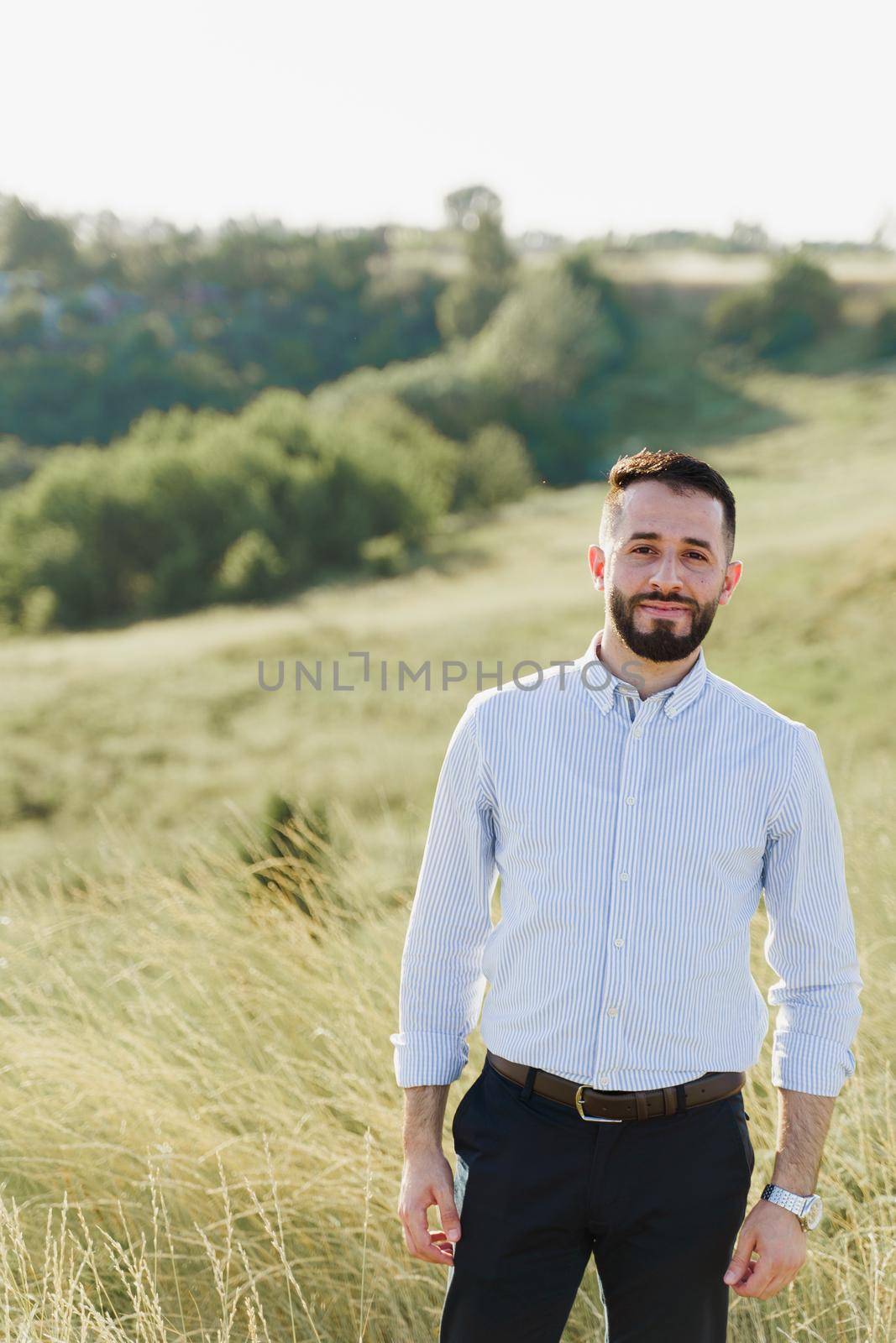Handsome bearded arabian man in sunglasses on the green hills background. Confident muslim business man. Arab man weared in white shirt