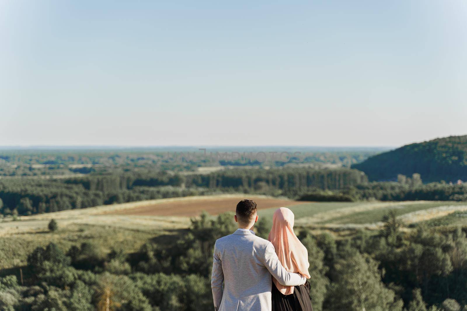 Muslim love story. Mixed couple smiles and hugs on the green hills . Woman weared in hijab looks to her man. Advert for on-line dating agency