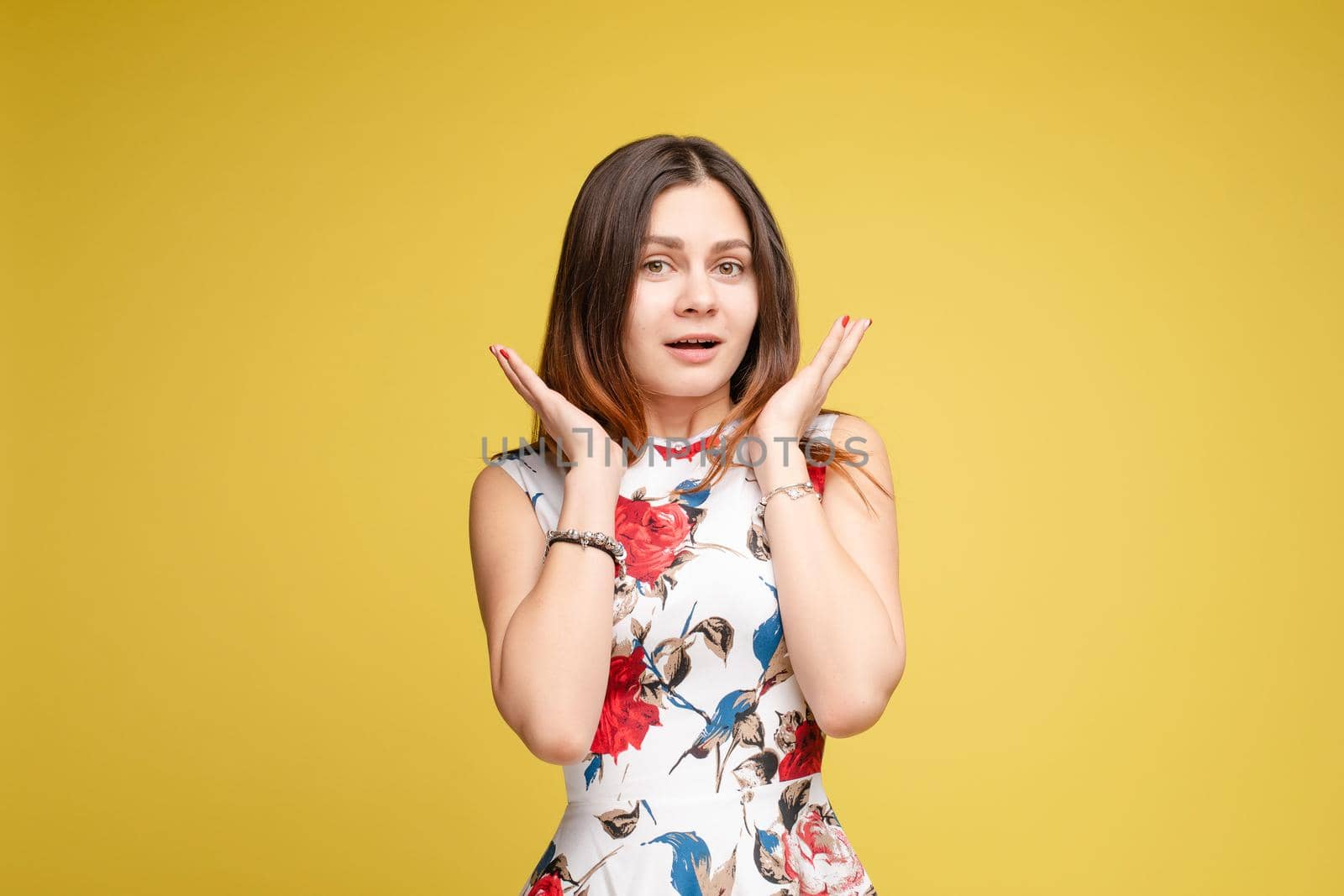 Front view of surprised young girl in bright dress looking at camera on yellow isolated background in studio. Funny amazed female with open eyes shouting. Concept of shock and happiness.
