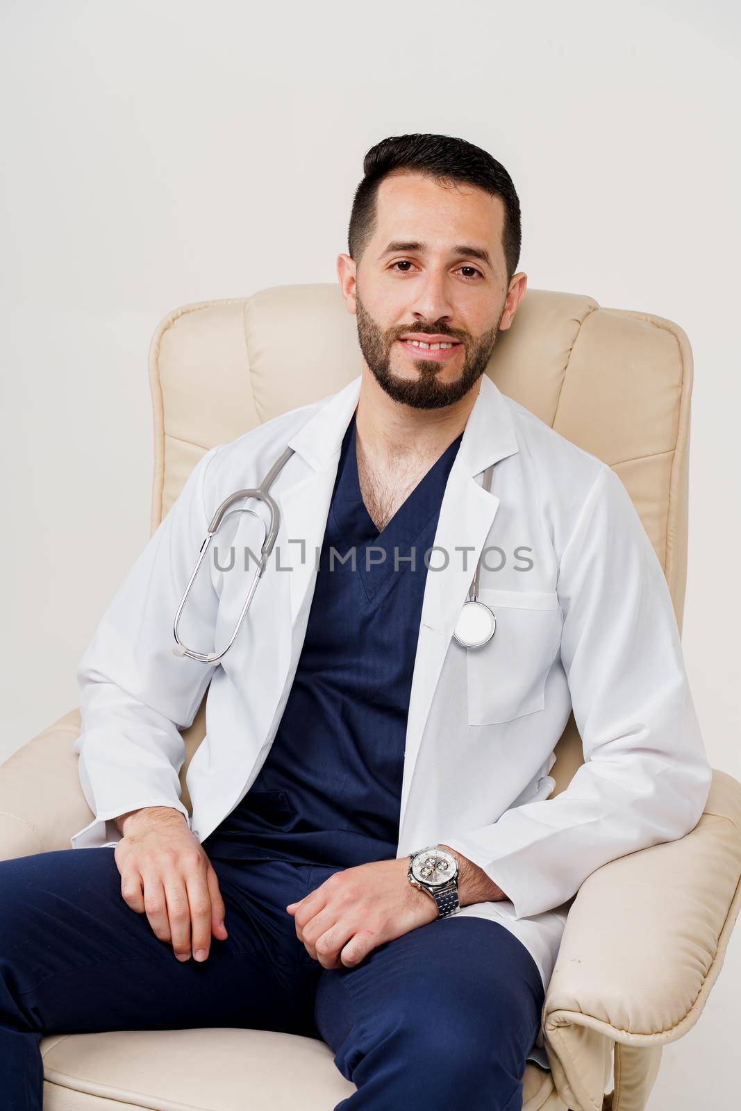 Arabian doctor surgeon in medical robe with phonendoscope seats in armchair in studio on white blanked background. Confident arab on white background. by Rabizo