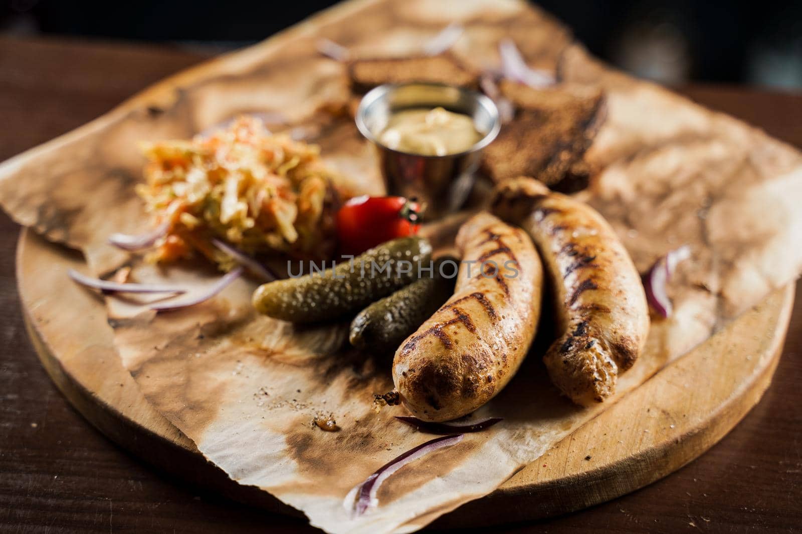 Grilled sausages with beer and vegetables with pickled cucumber, cabbage salad sauce and bread on parchment, top view.