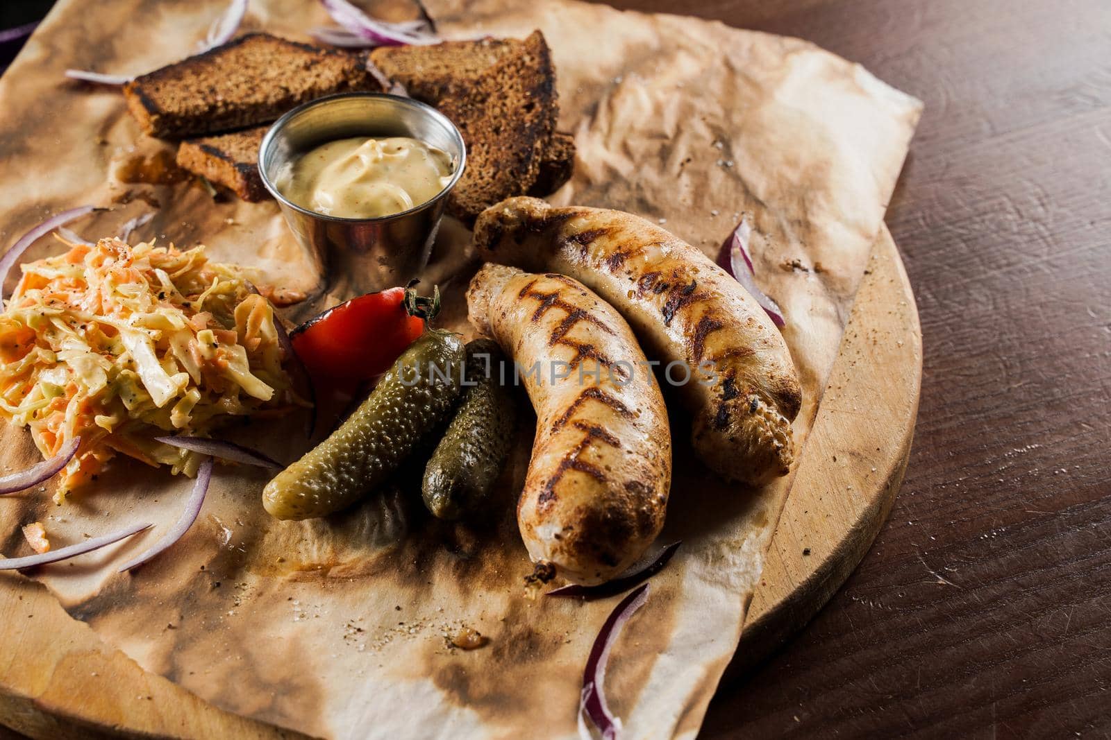 Grilled sausages with beer and vegetables with pickled cucumber, cabbage salad sauce and bread on parchment, top view.