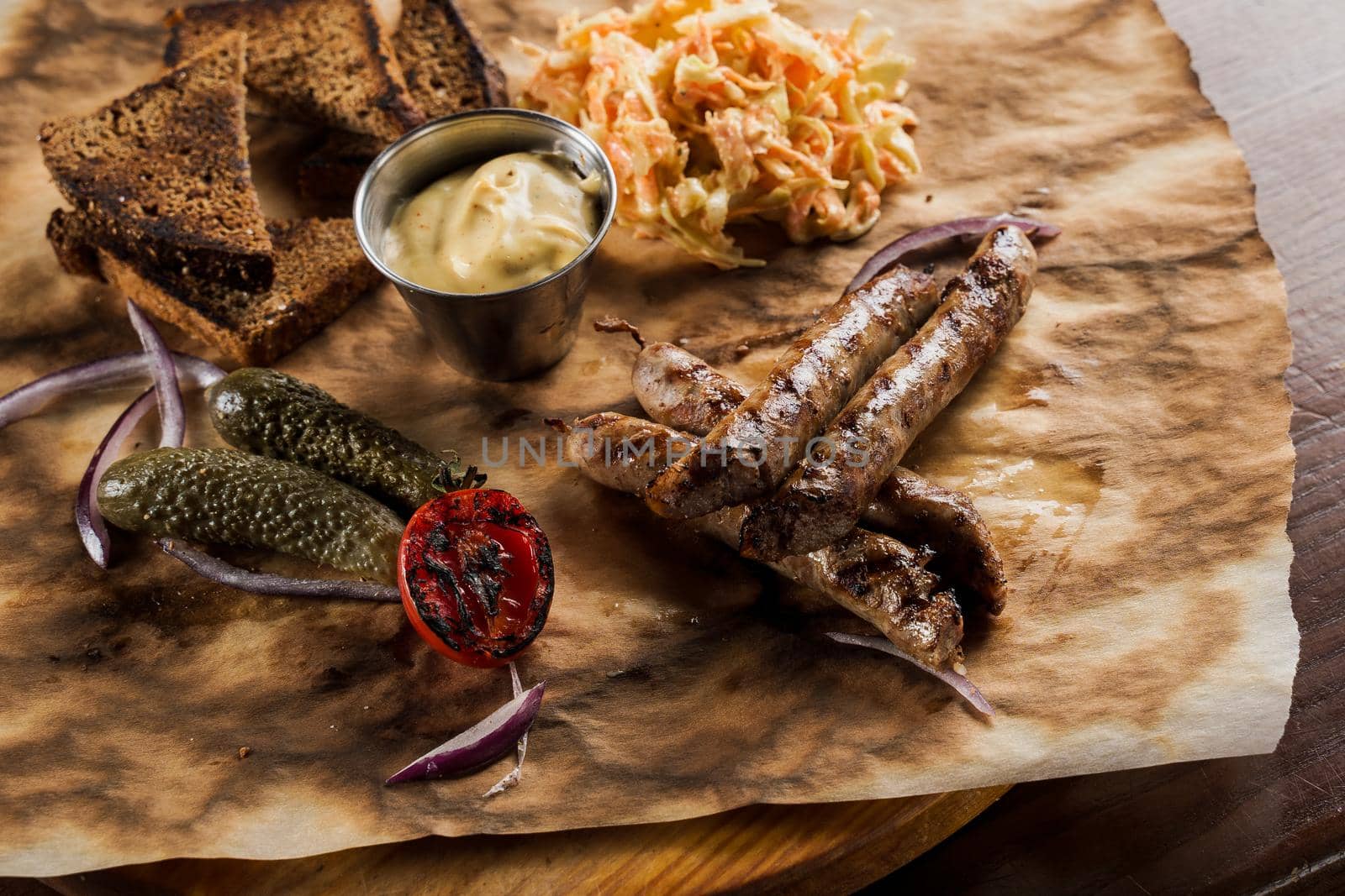 Grilled sausages with beer and vegetables with pickled cucumber, cabbage salad sauce and bread on parchment, top view.