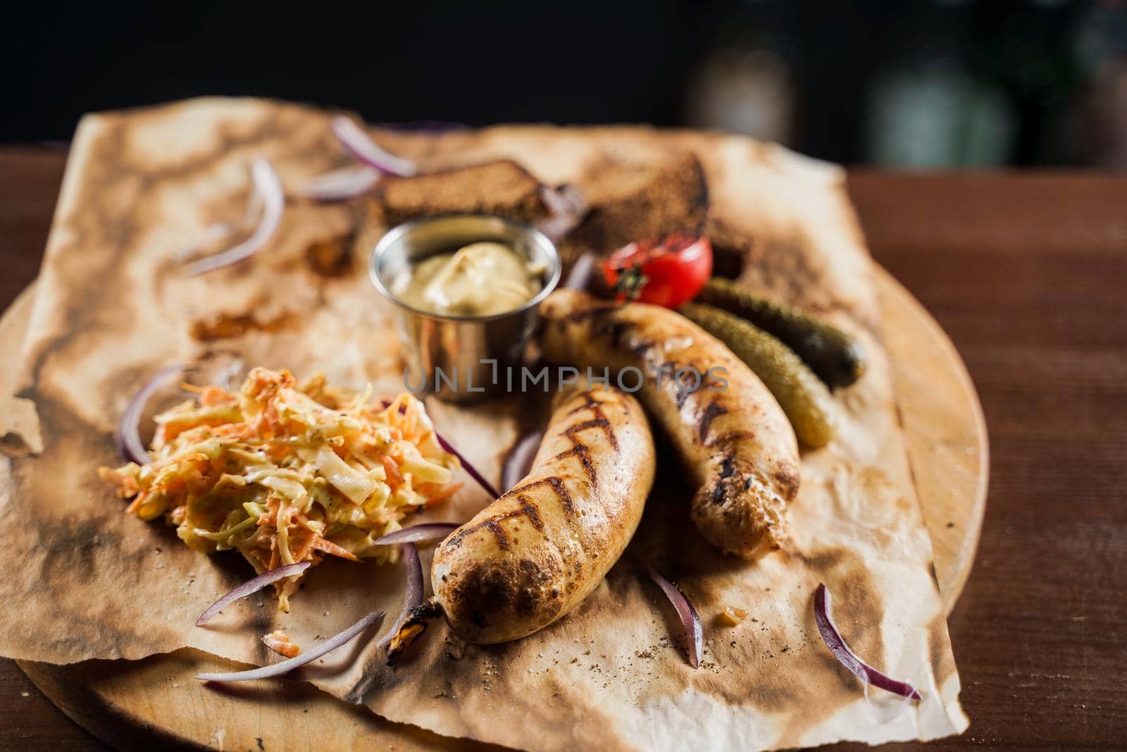 Grilled sausages with beer and vegetables with pickled cucumber, cabbage salad sauce and bread on parchment, top view.