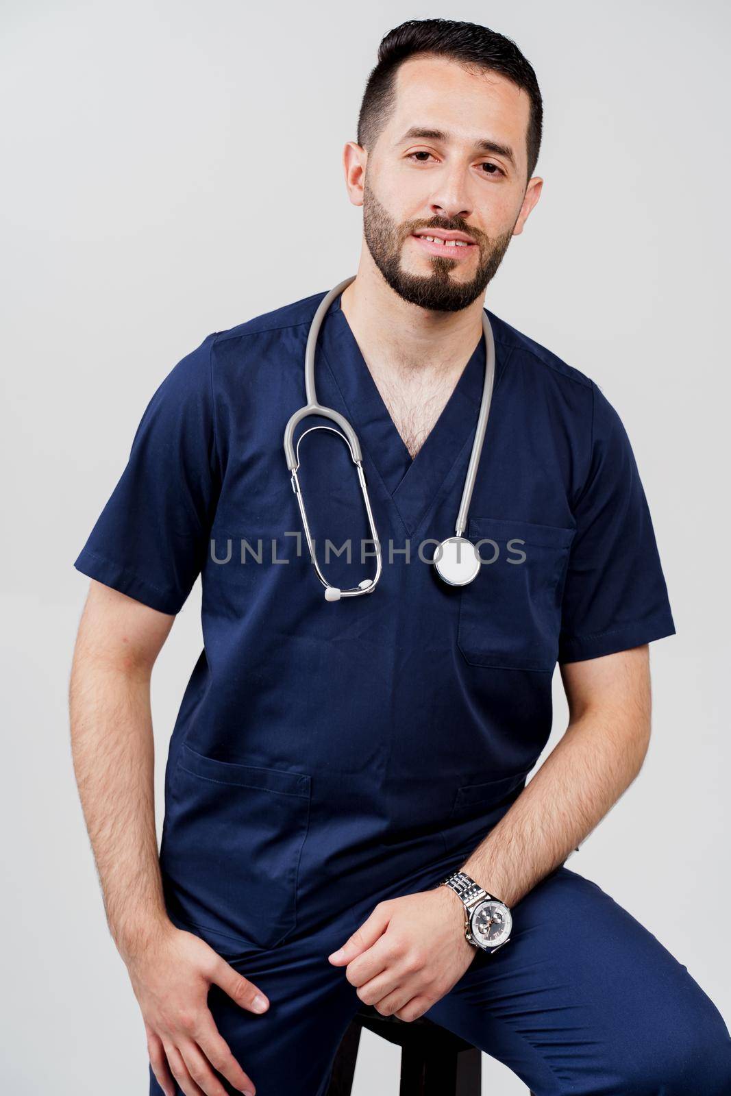 Arabian medical student with stethoscope in surgical uniform. Handsome bearded man in studio. Confident doctor at consultation