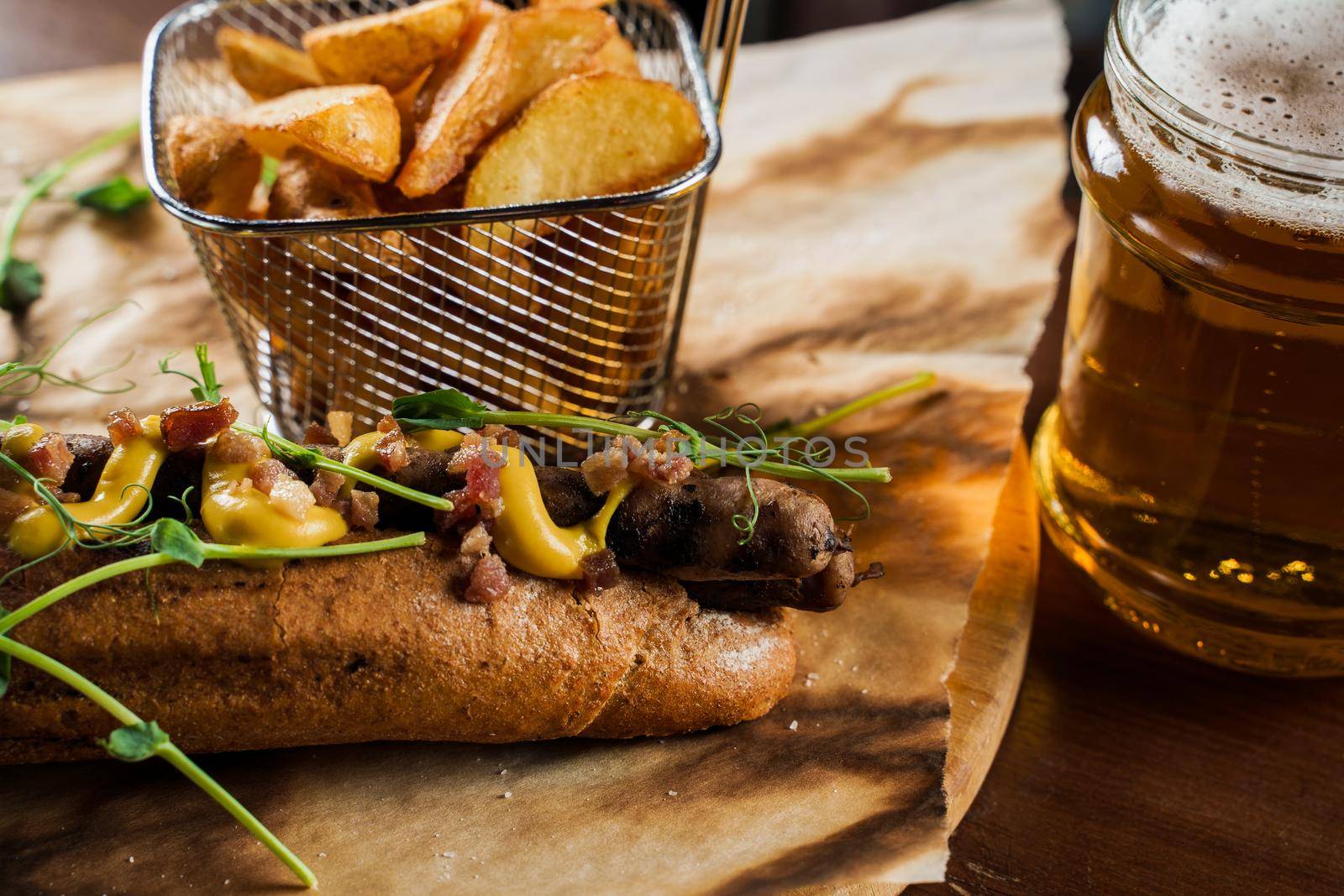 Barbecue grilled hot dog and beer with yellow mustard and ketchup on wooden background. Hot dog sandwich with potato fries and sauces.