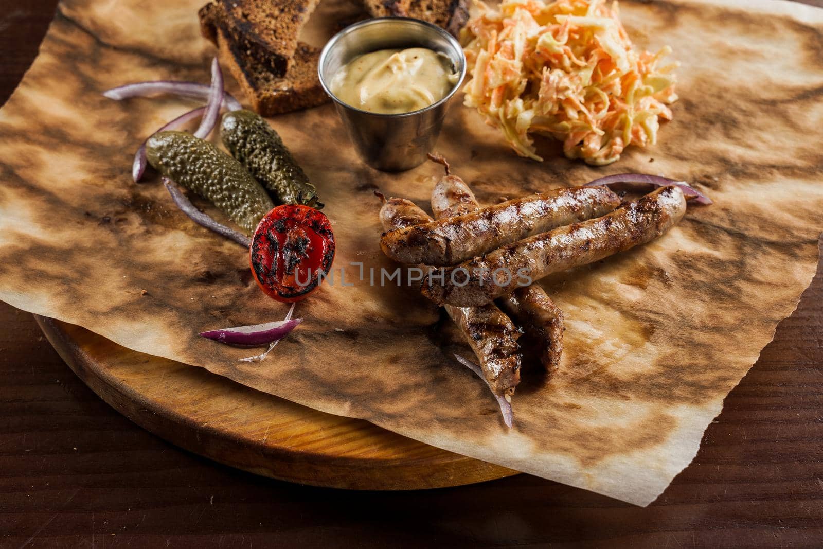 Grilled sausages with beer and vegetables with pickled cucumber, cabbage salad sauce and bread on parchment, top view by Rabizo