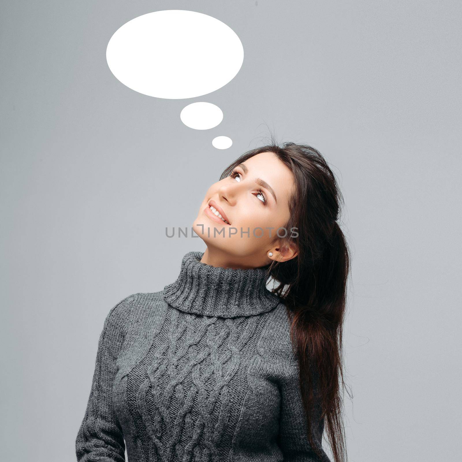 Waist up portrait of happy dreaming pretty woman with amazing long hair and nice smile. Beautiful female posing at studio in fashionable sweater. Isolated on gray background