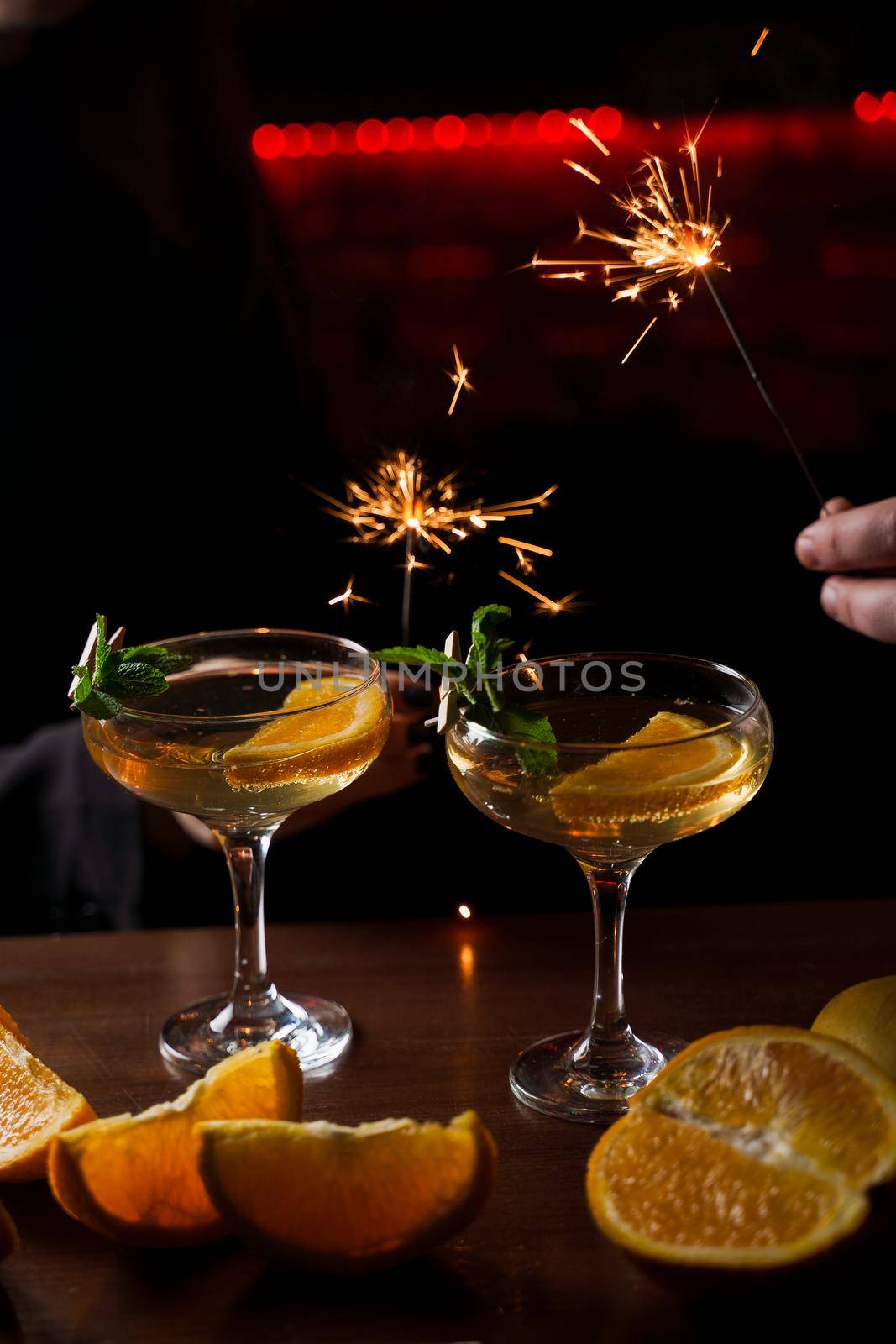 Celebrating new year eve 2022 with sparklers fireworks and drinking cocktails. Mint with orange slice in a cocktail glass filled with alcohol cocktails.