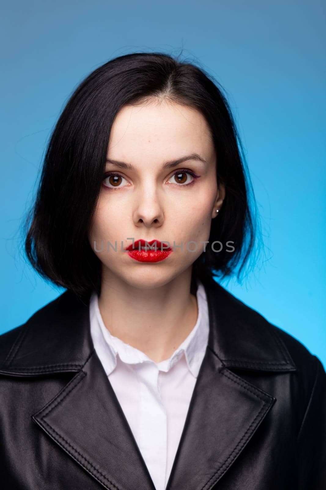 brunette woman with red lipstick on her lips in a black leather jacket and white shirt, blue background by shilovskaya