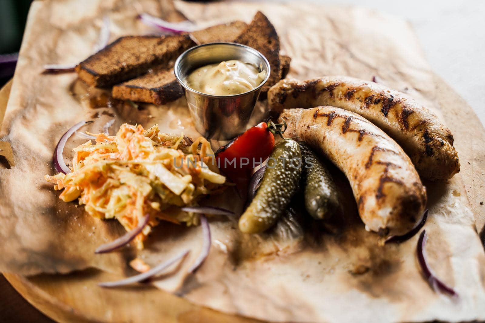 Grilled sausages with beer and vegetables with pickled cucumber, cabbage salad sauce and bread on parchment, top view.