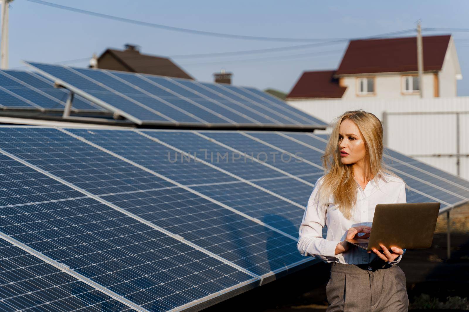 Investor and solar panels. Blonde woman with laptop near blue solar panels row on ground. electricity for home. Sustainability of planet. Green energy.