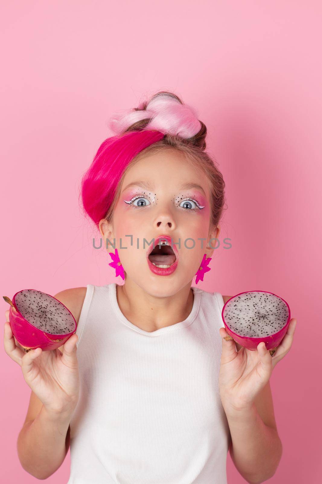 Close-up portrait of pretty girl with pink hairstyle with dragon fruit on pink background. Studio shot of charming tween girl with pink make up enjoying juicy red pitaya. exotic Pitahaya fruit by oliavesna