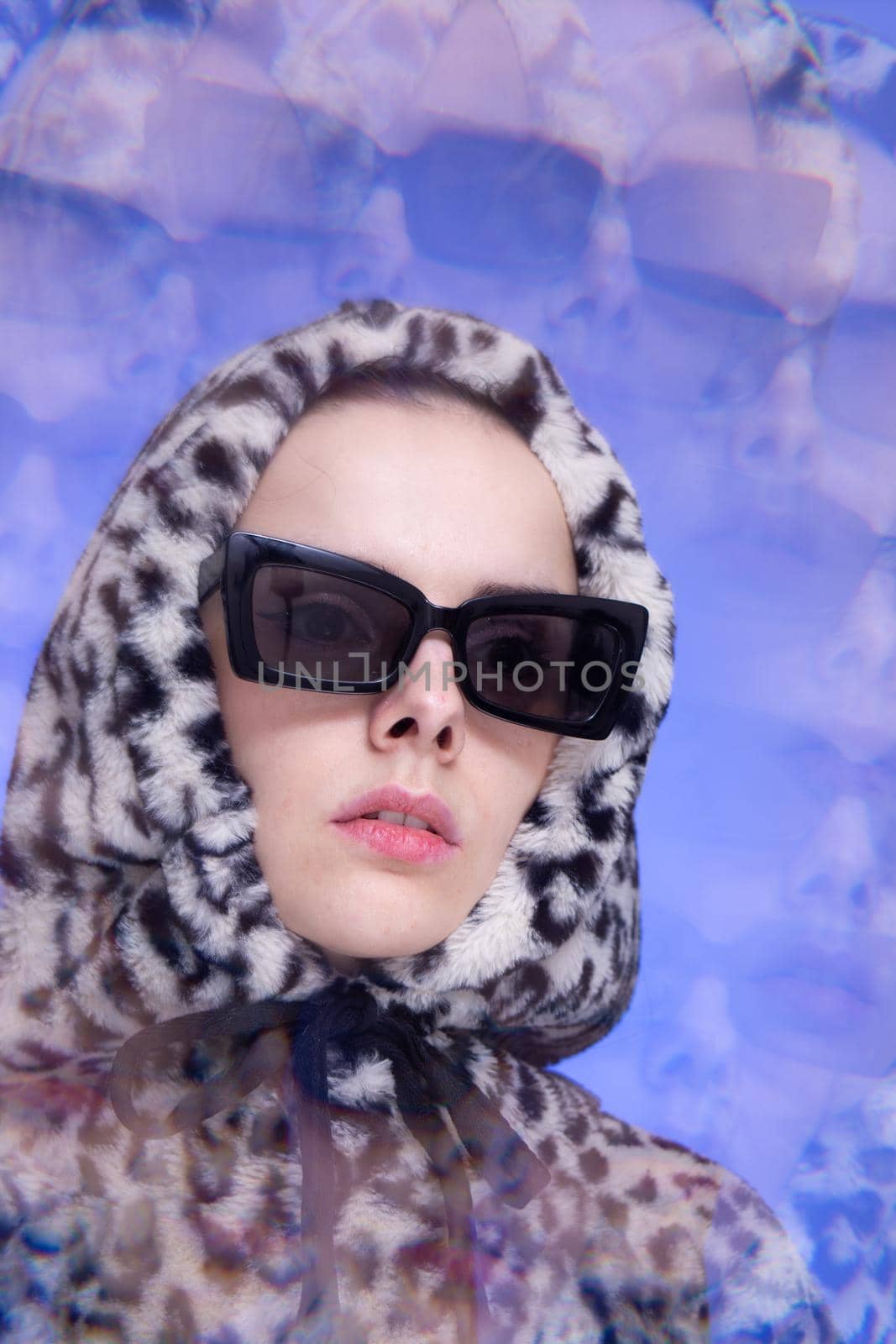 Art portrait, a woman in black glasses and a leopard hoodie on a blue background. High quality photo