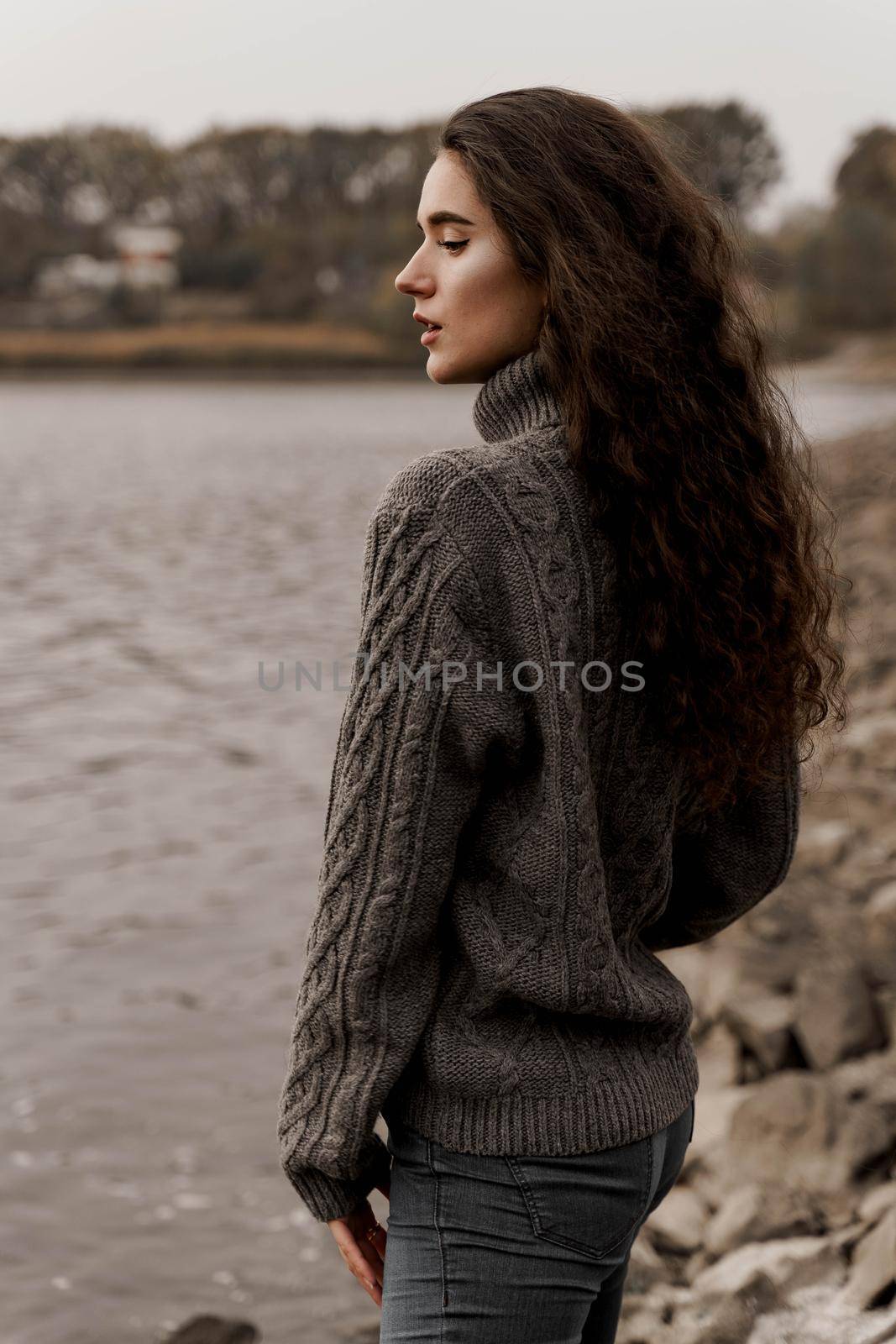 Girl with curly hair on the background of birch with stones and lake in autumn. by Rabizo