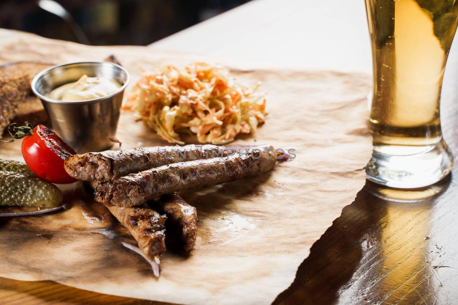 Grilled sausages with beer and vegetables with pickled cucumber, cabbage salad sauce and bread on parchment, top view.