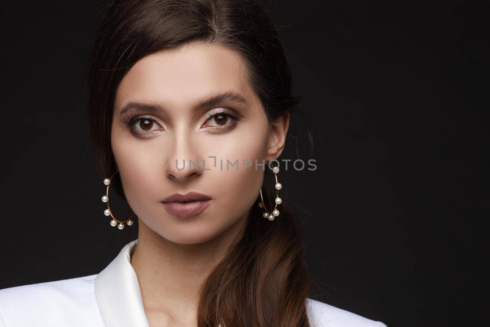 Close up of gorgeous and seductive woman with perfect bronze clean skin, plumps lips, confident looking at camera. Young brunette girl after procedure and makeup in beauty salon. Concept of beauty.