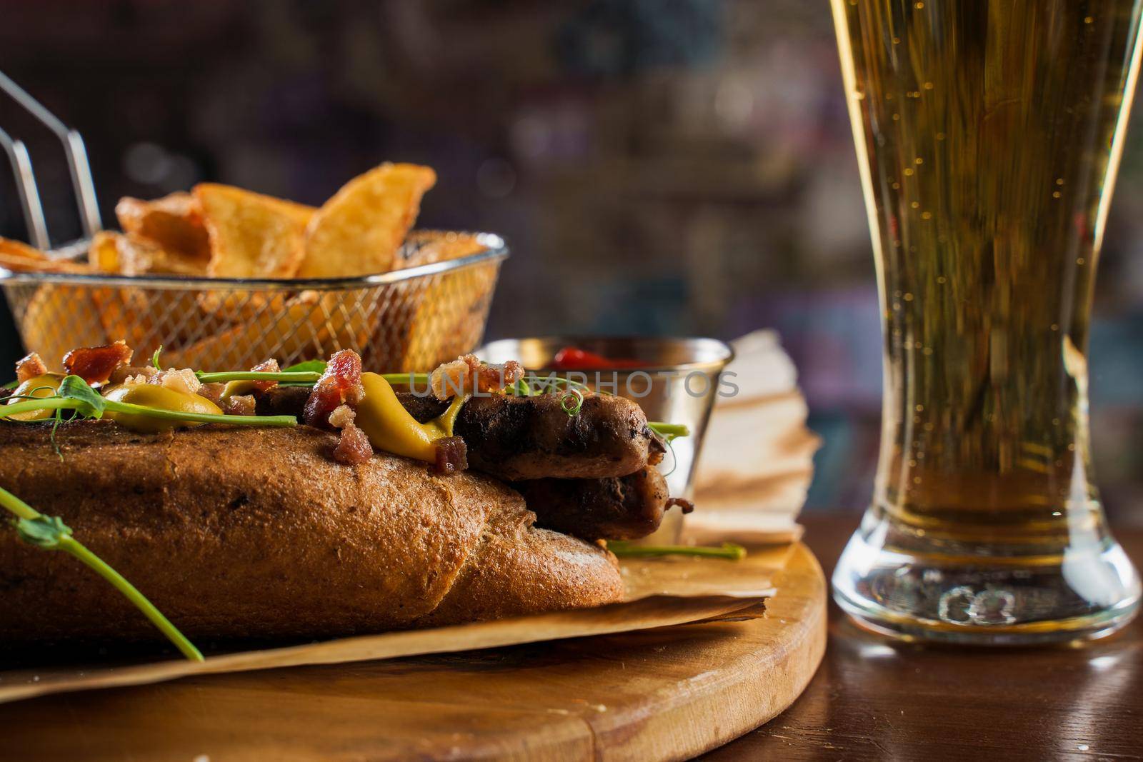 Barbecue grilled hot dog and beer with yellow mustard and ketchup on wooden background. Hot dog sandwich with potato fries and sauces.