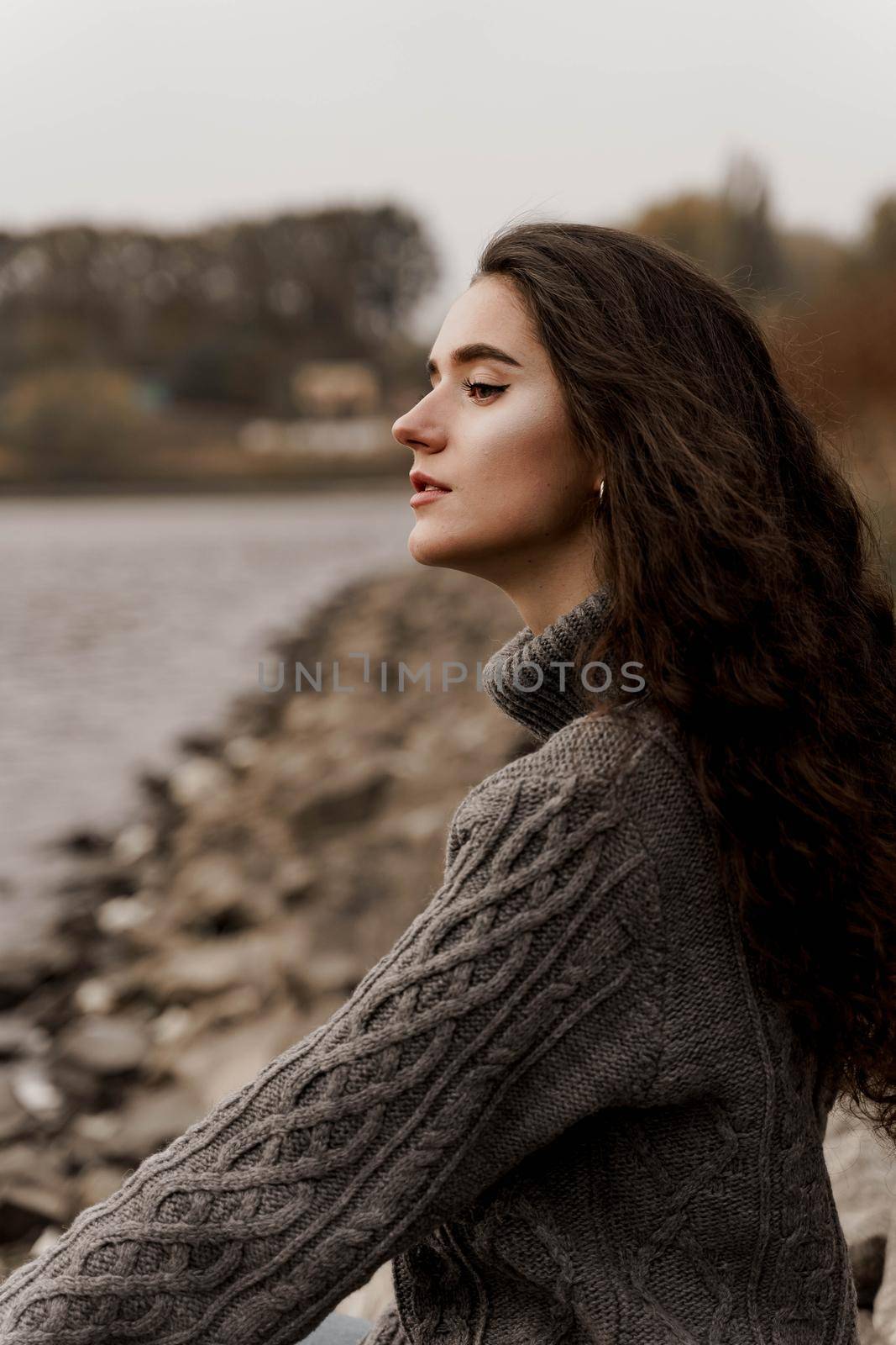 Girl with curly hair on the background of birch with stones and lake in autumn.