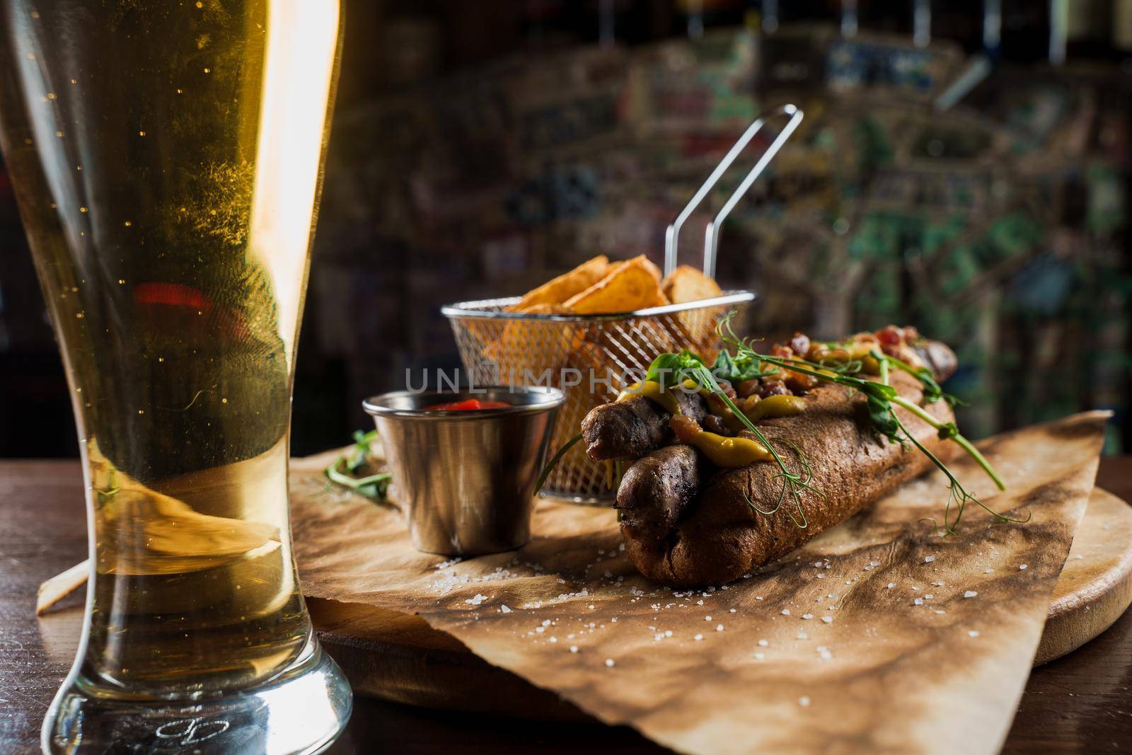 Barbecue grilled hot dog and beer with yellow mustard and ketchup on wooden background. Hot dog sandwich with potato fries and sauces.