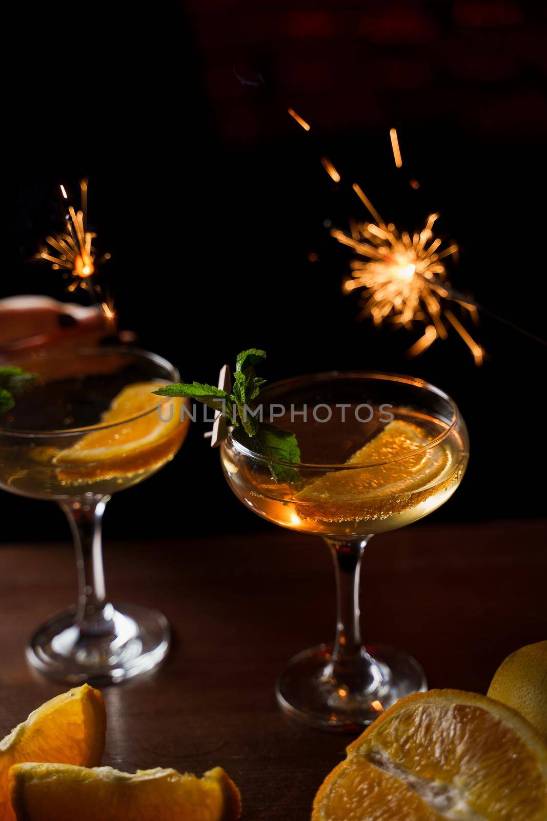 Celebrating new year eve 2022 with sparklers fireworks and drinking cocktails. Mint with orange slice in a cocktail glass filled with alcohol cocktails.