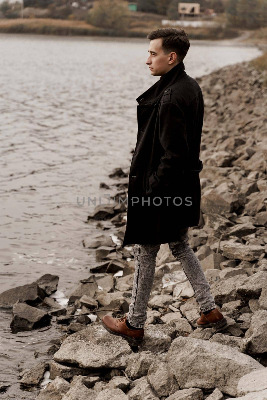 Confident business man walks near lake and thinks about his business during quarantine coronavirus covid-19 period. Handsome male weared formal black coat
