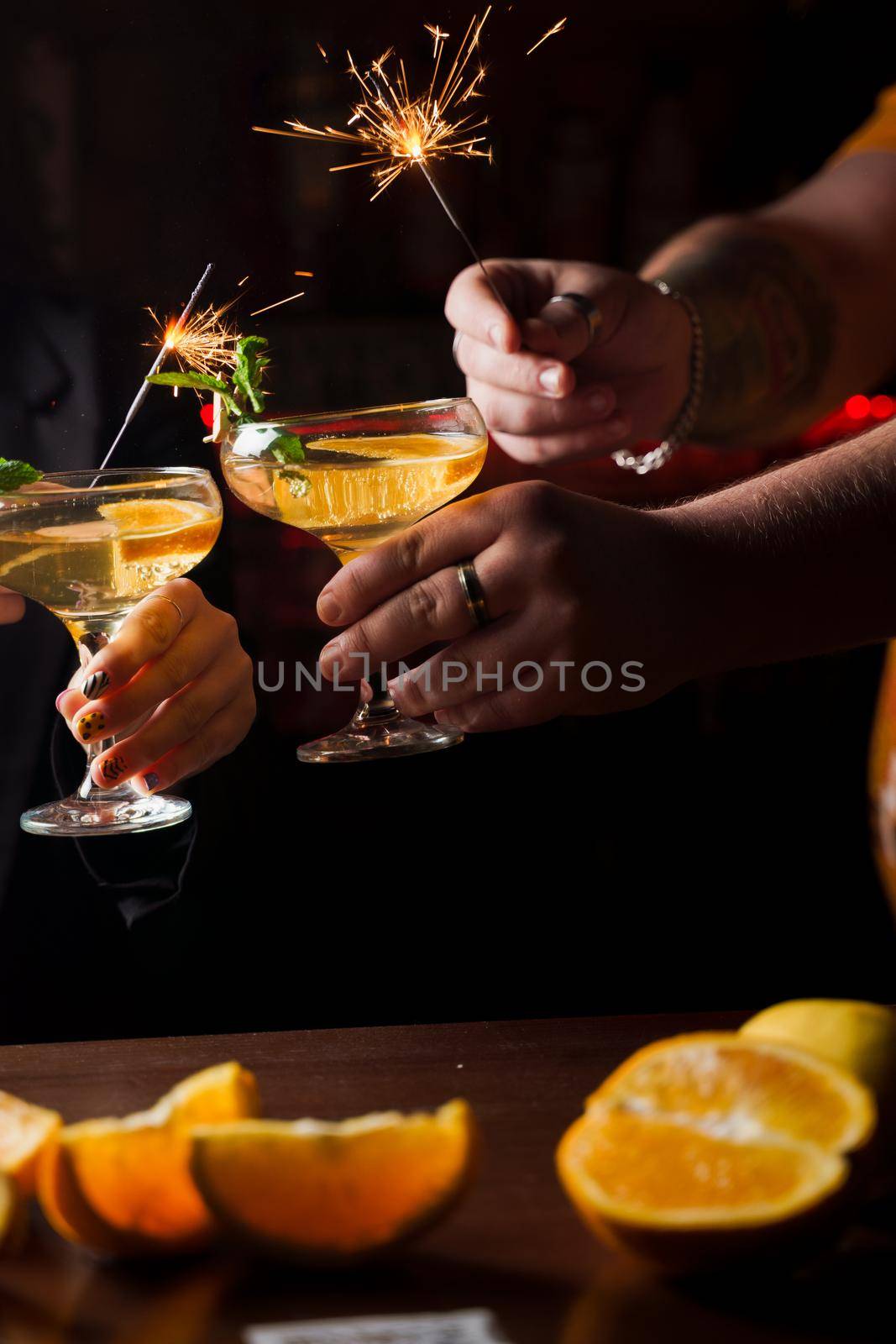 Celebrating new year eve 2022 with sparklers fireworks and drinking cocktails. Mint with orange slice in a cocktail glass filled with alcohol cocktails by Rabizo