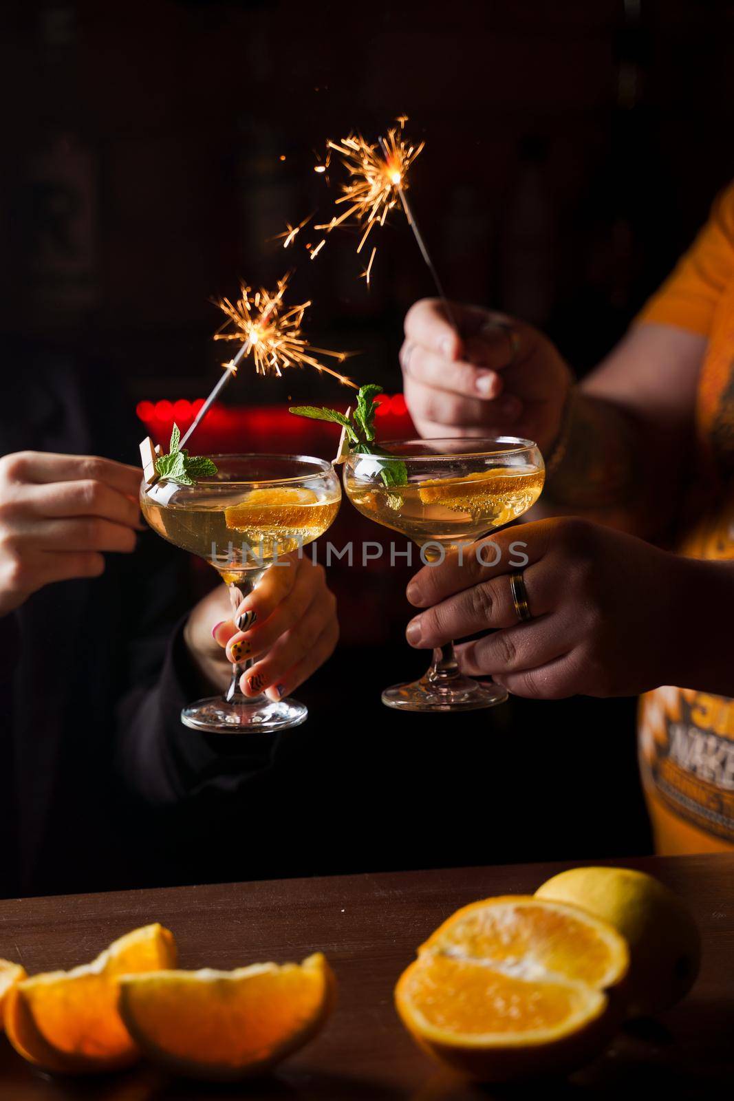 Celebrating new year eve 2022 with sparklers fireworks and drinking cocktails. Mint with orange slice in a cocktail glass filled with alcohol cocktails.